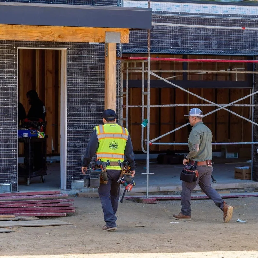Electricians walk through a commercial tenant improvement construction site with scaffolding, exposed framing, and unfinished interiors, illustrating electrical buildout work during a commercial renovation project.
