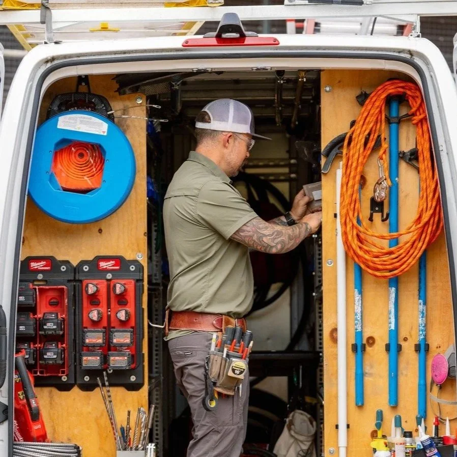 Electrician organizing equipment inside a service van, preparing for a home battery backup installation involving electrical panel connections, transfer switches, wiring upgrades, and residential energy storage systems.