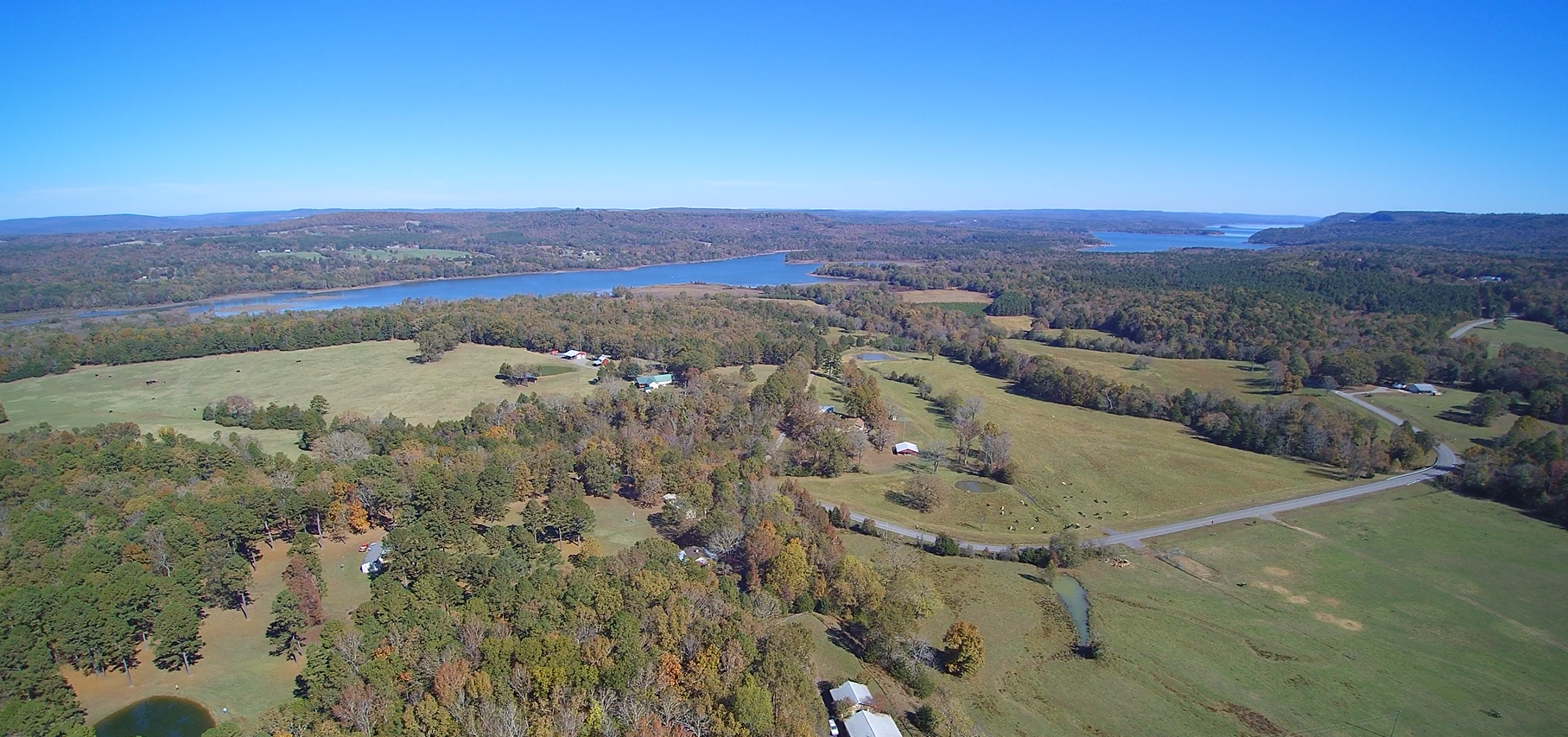 Aerial view of a Van Buren County with a large lake, rolling green fields, scattered trees, winding roads, and farm buildings under a clear blue sky.
