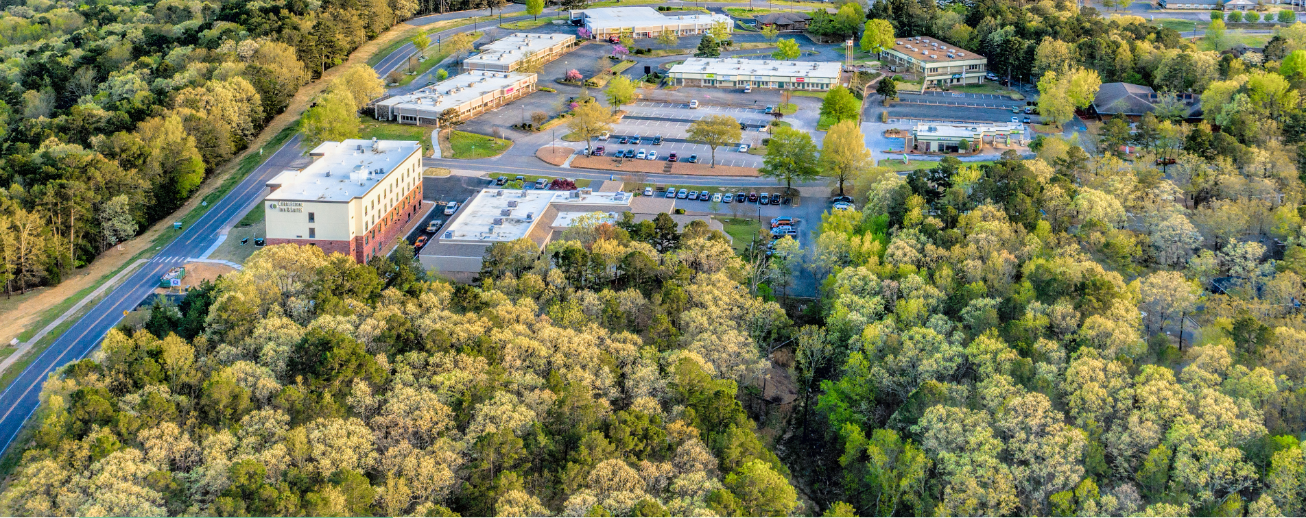Aerial view of a commercial office complex surrounded by forest, with parking lots, roads, and multiple buildings.
