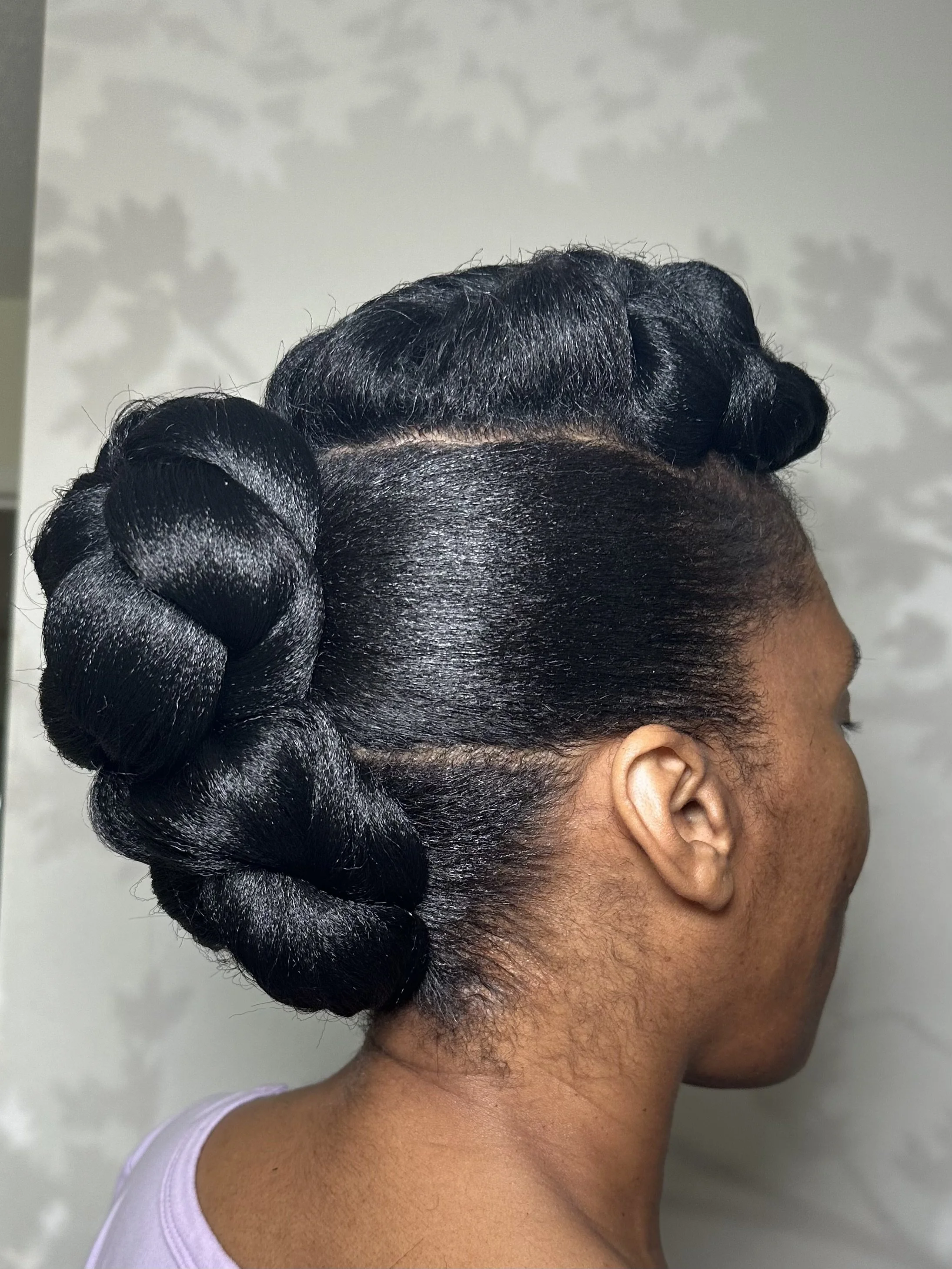 A woman with black hair styled in vintage finger waves and a large braided bun at the back of her head.