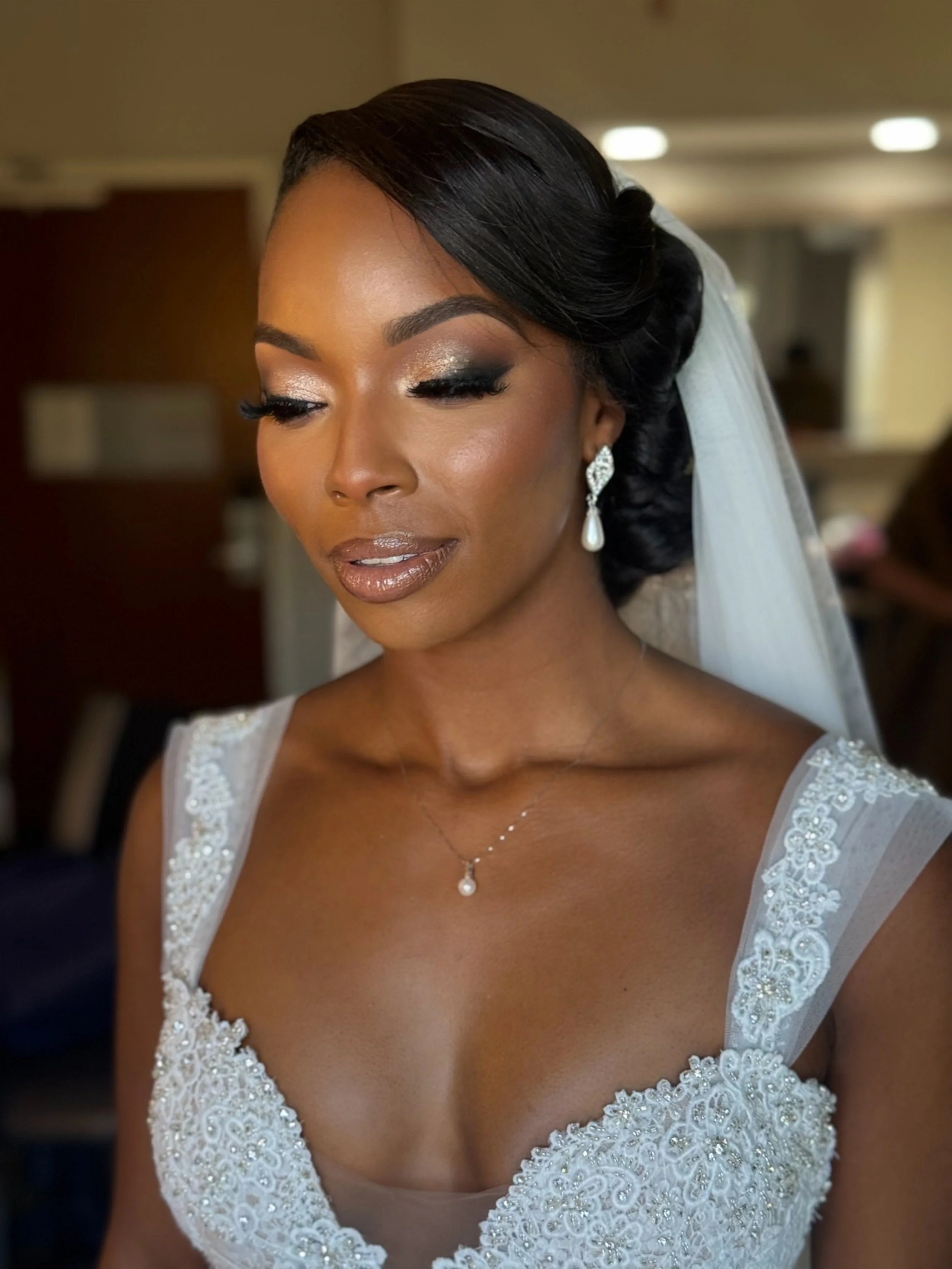 Close-up of a bride on her wedding day, wearing a white lace gown with intricate embroidery, teardrop earrings, and a pearl necklace, with her hair styled in an elegant updo.