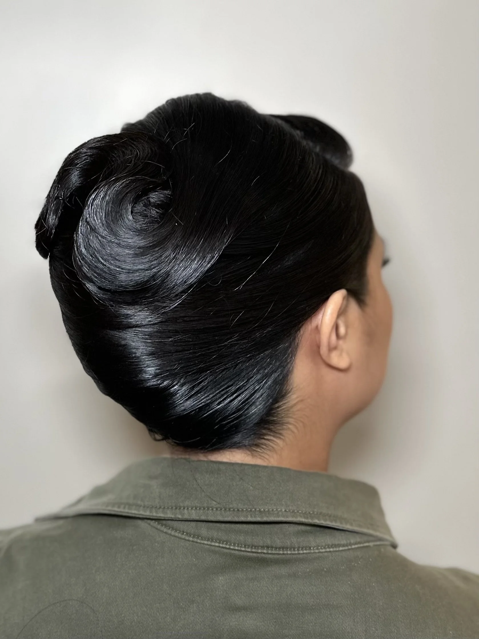 Close-up of a woman with vintage-style, black, shiny, pinned-up hairdo.