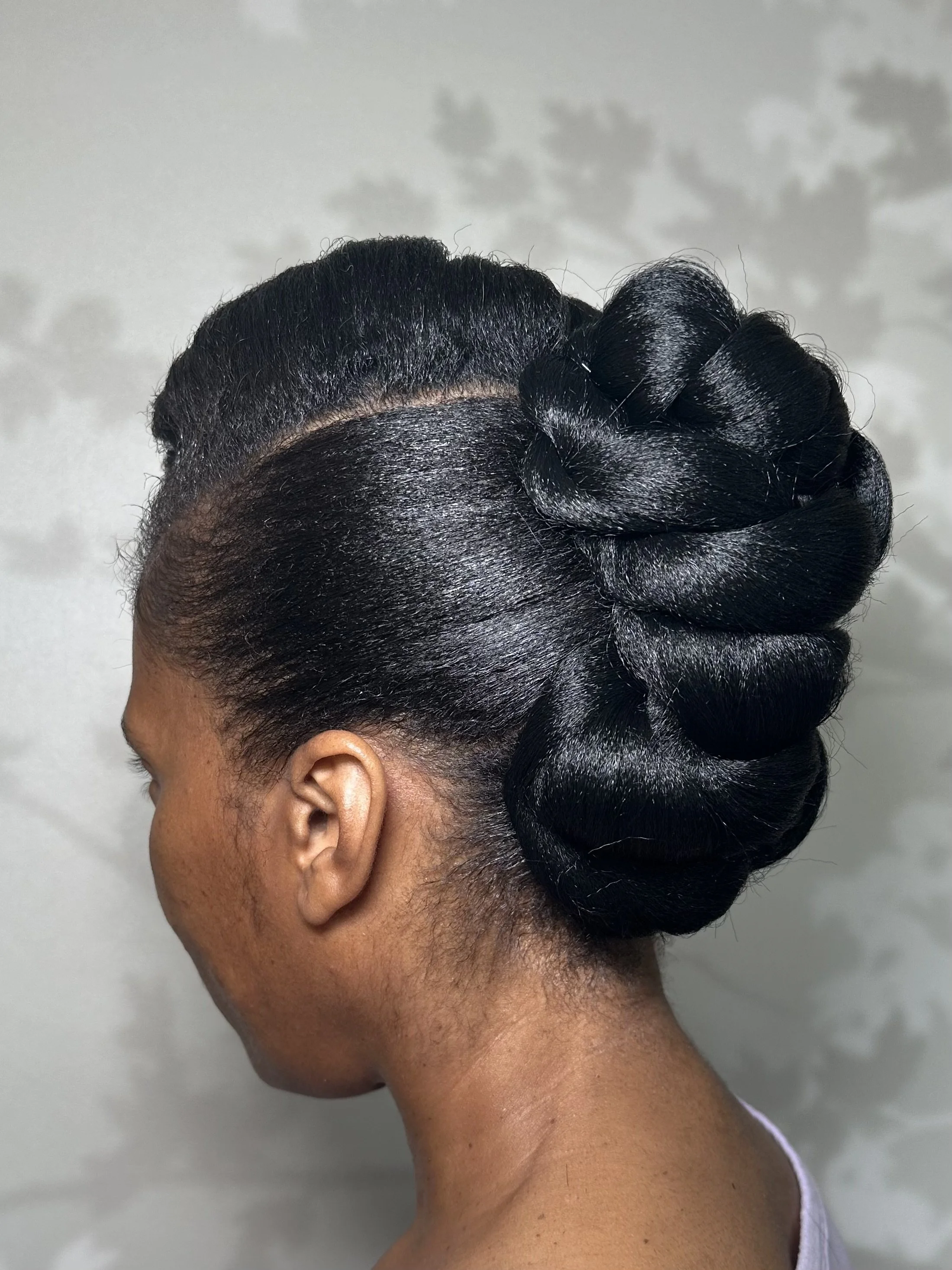 Close-up of a woman's head, showcasing an elegant updo hairstyle with glossy, styled hair twisted into a large, intricate bun at the back.