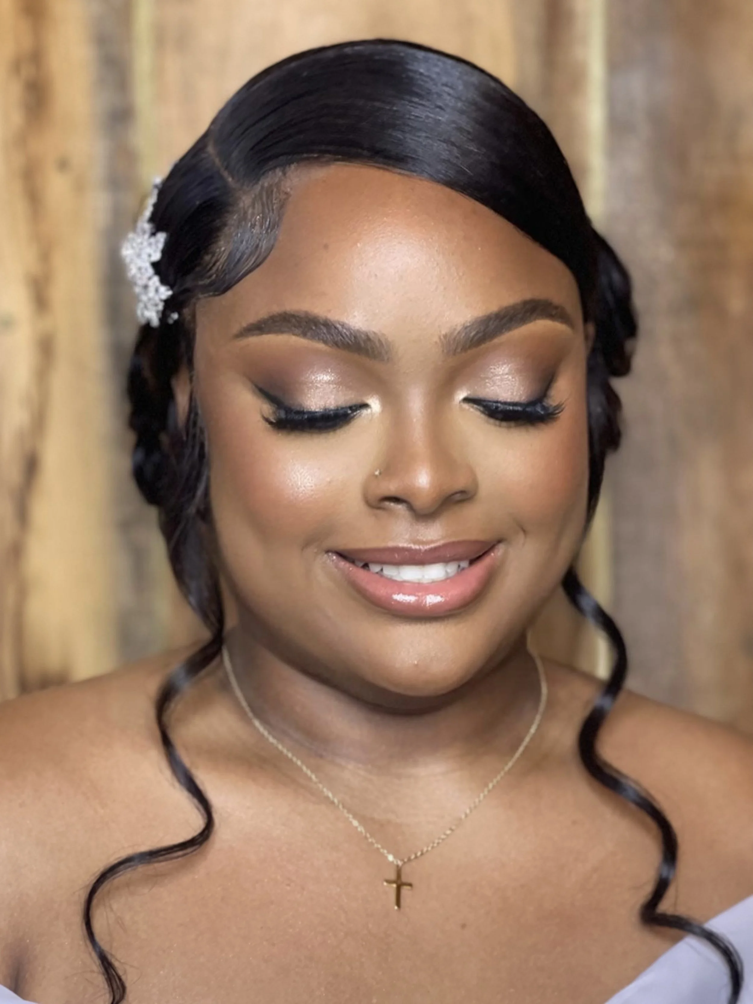 Close-up of a woman with dark, styled hair, wearing makeup, a gold cross necklace, and a white top.