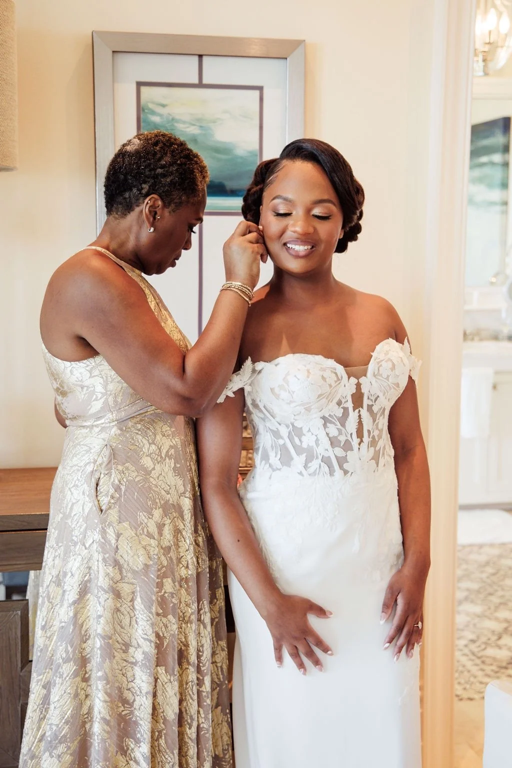 A bride getting ready on her wedding day with a woman helping her put on earrings.
