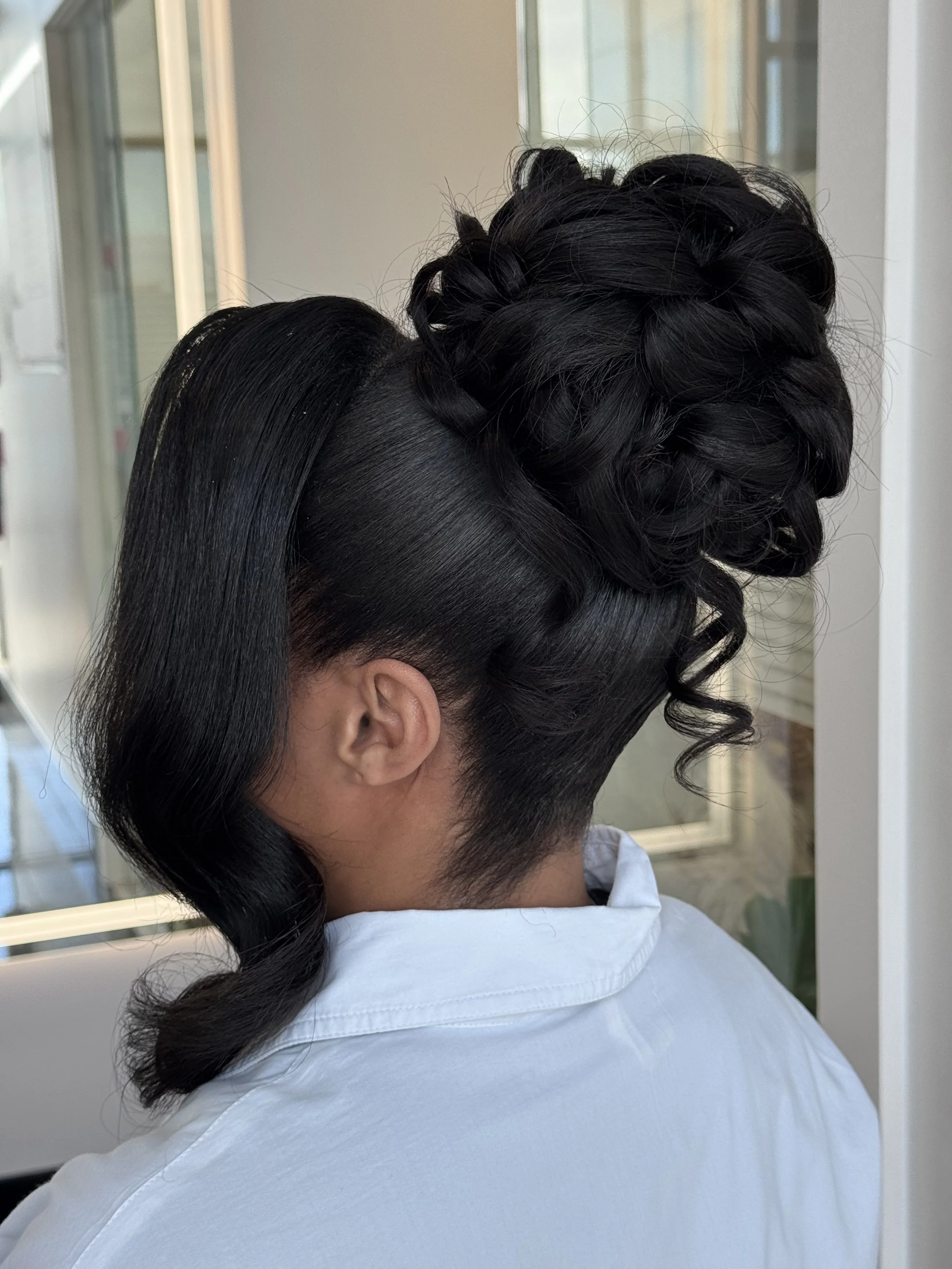 Close-up of a person's hairstyle featuring a sleek, shiny section of straight black hair and an intricate updo with curled and braided elements.