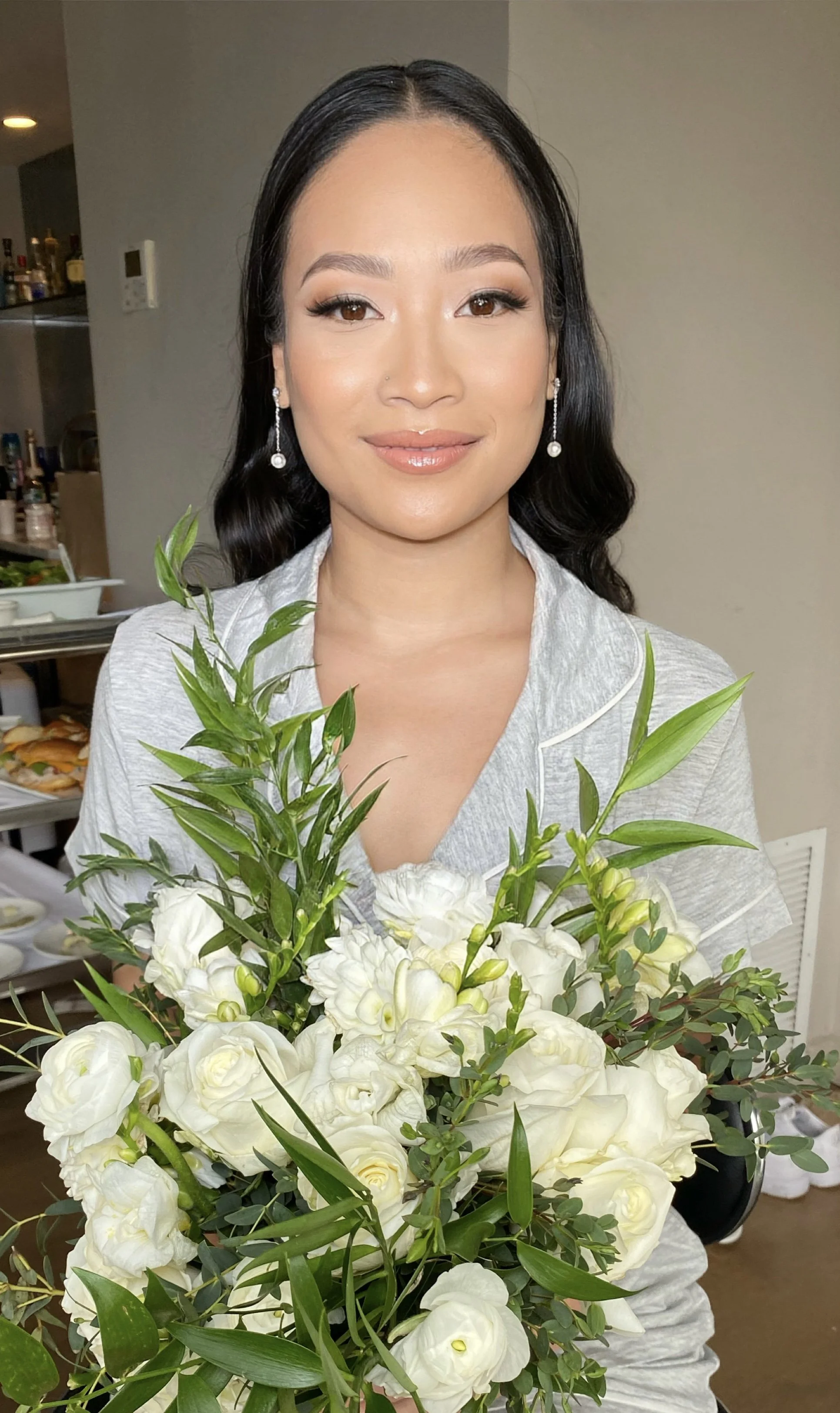 A woman with dark hair and earrings holding a large bouquet of white flowers with green leaves.