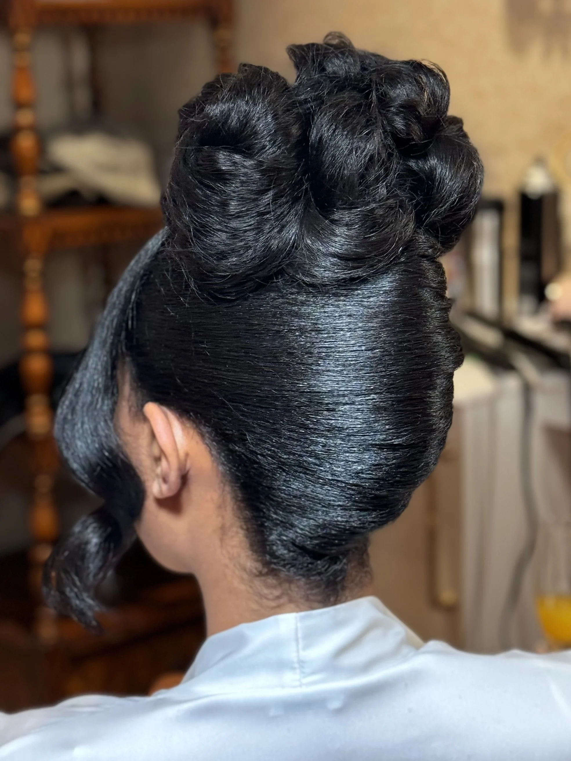 Close-up of a hairstyle featuring vintage finger waves and a sleek, smooth finish, worn by a person with dark, shiny hair.