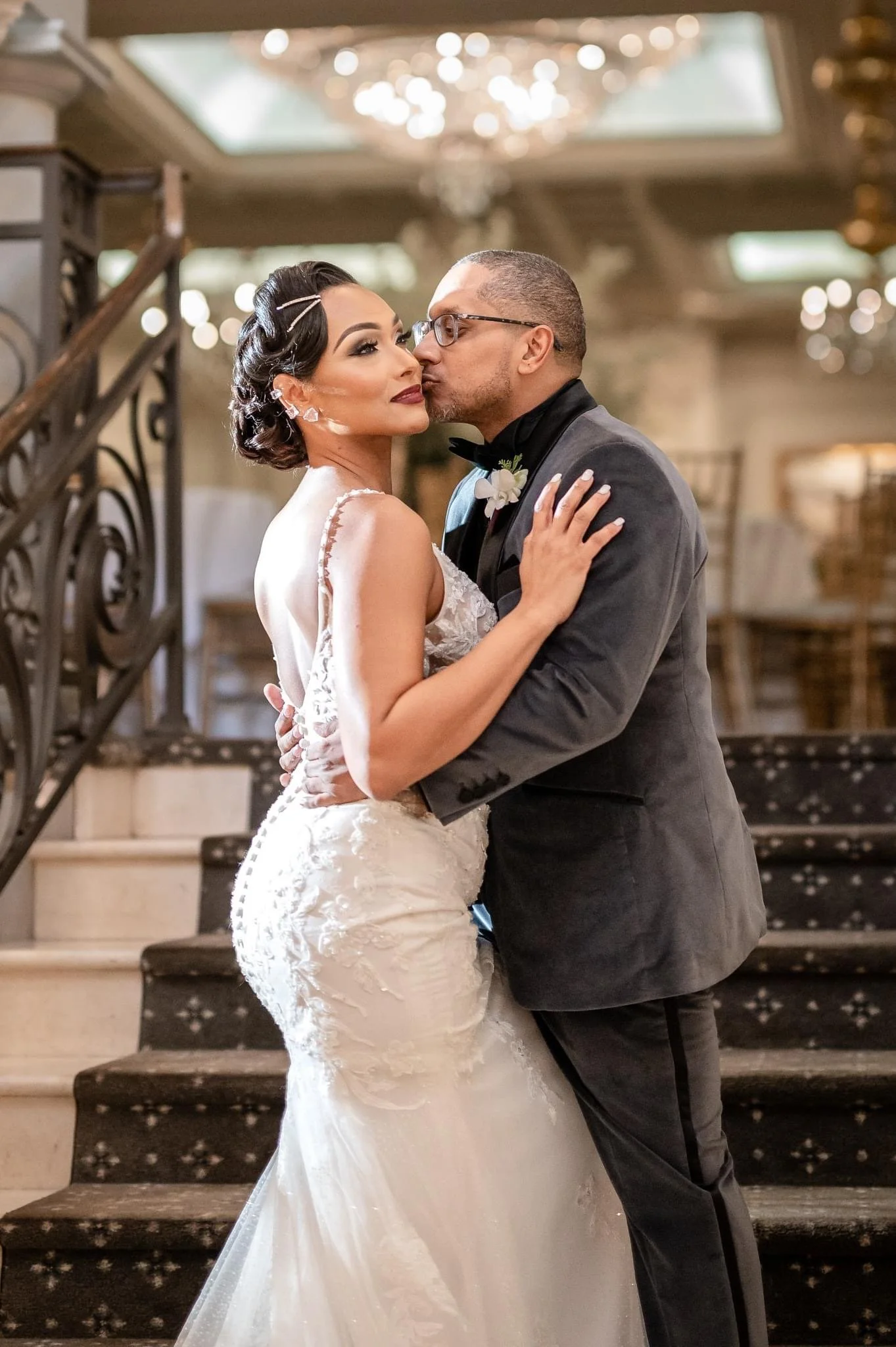 A bride and groom sharing a kiss on a staircase during their wedding reception in an elegant venue.
