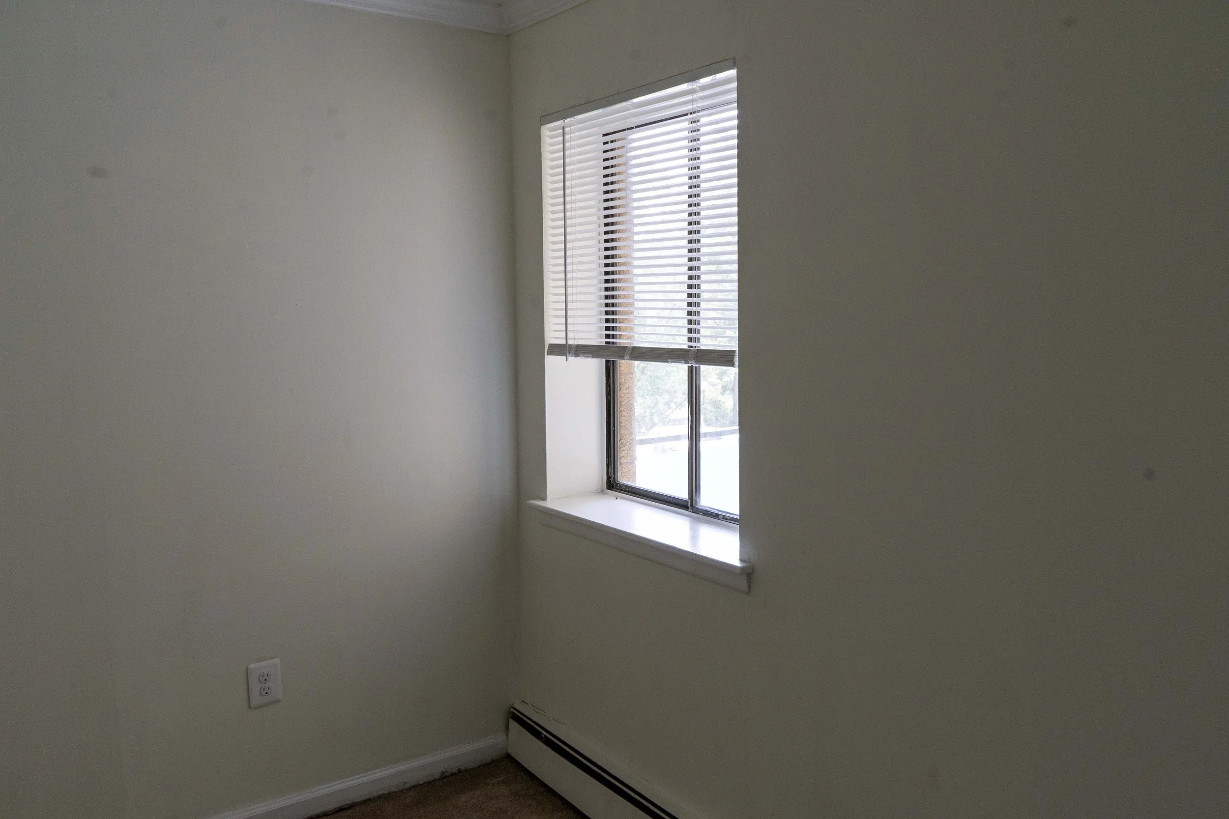 Empty room with a window, beige walls, and a baseboard heater.