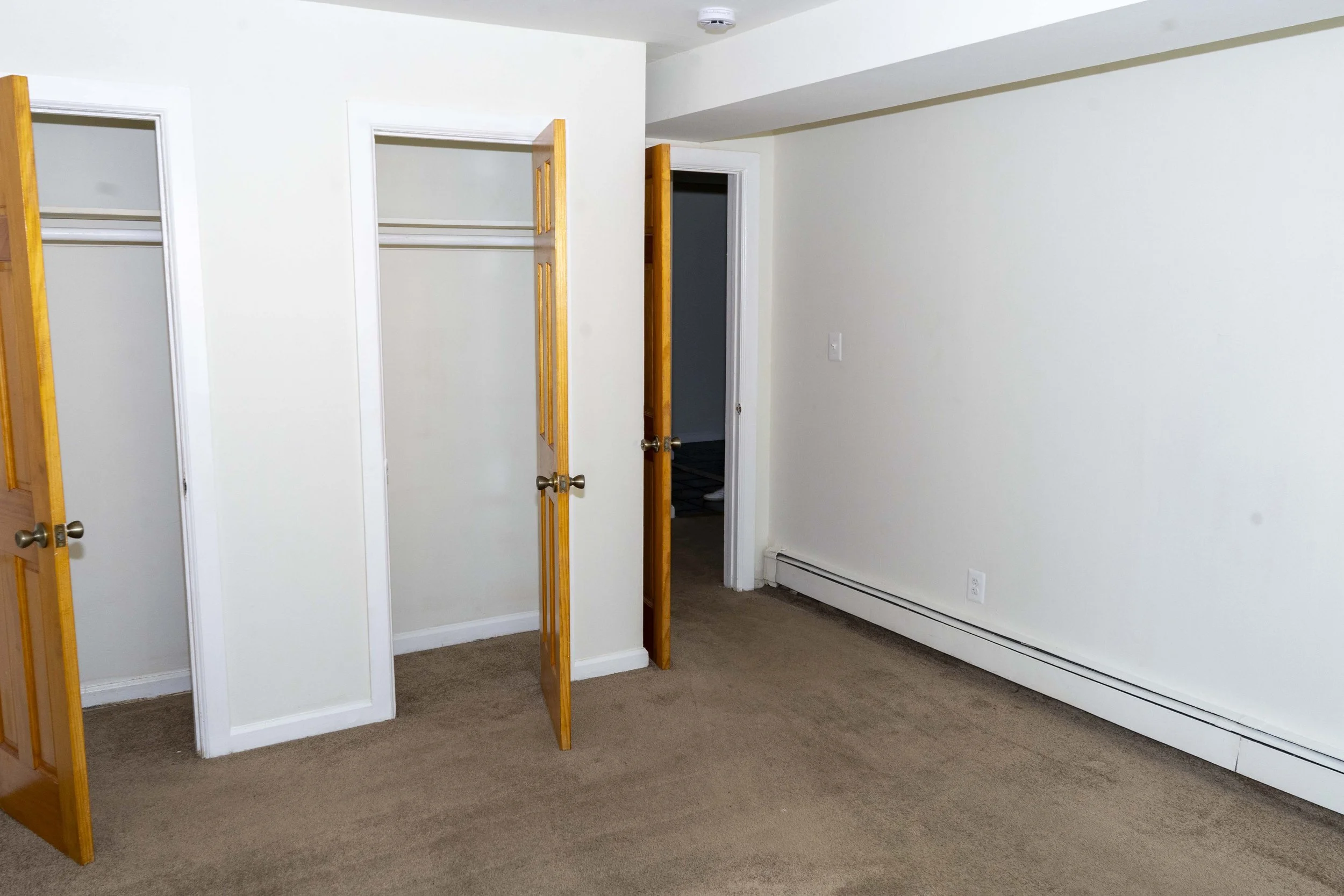 Empty room with beige carpet, white walls, open closet doors, and a partially open door leading to a bathroom.