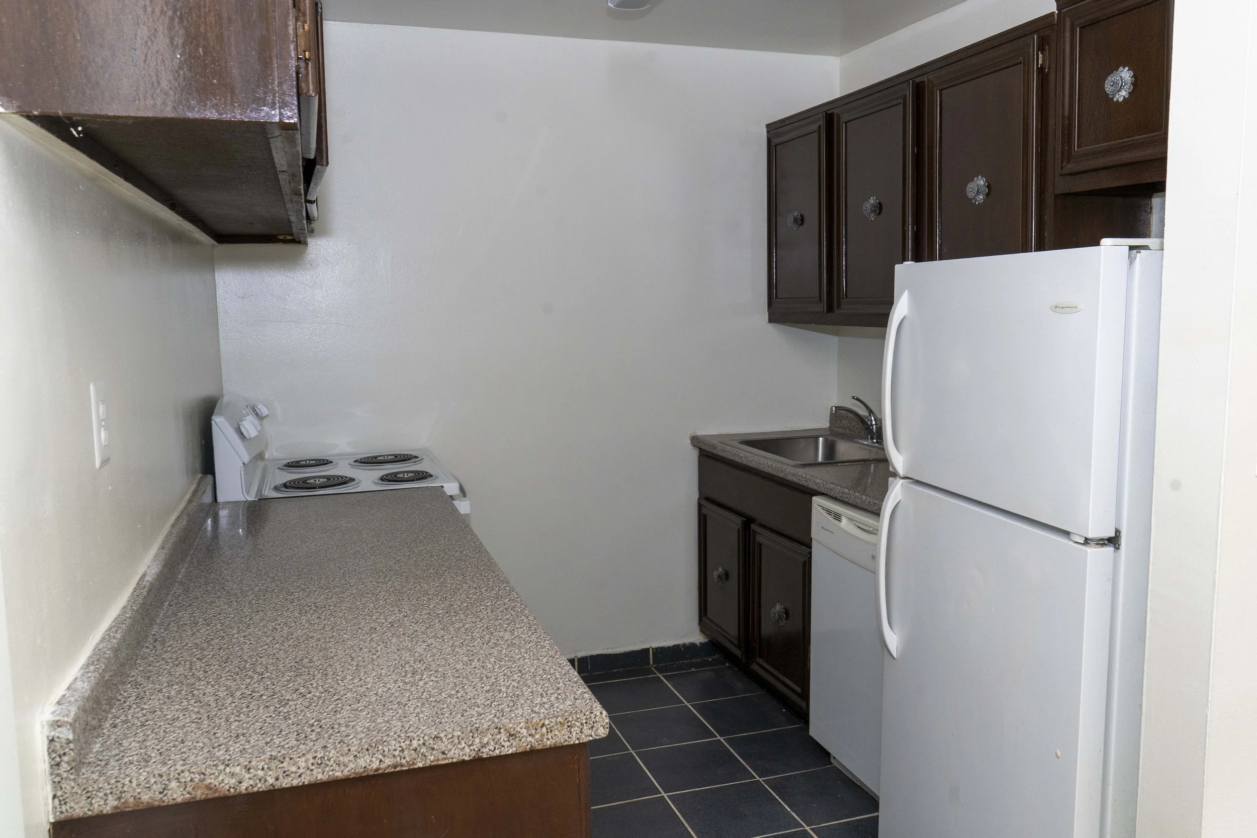 Small kitchen with dark brown cabinets, white refrigerator, and white stove with coil burners.