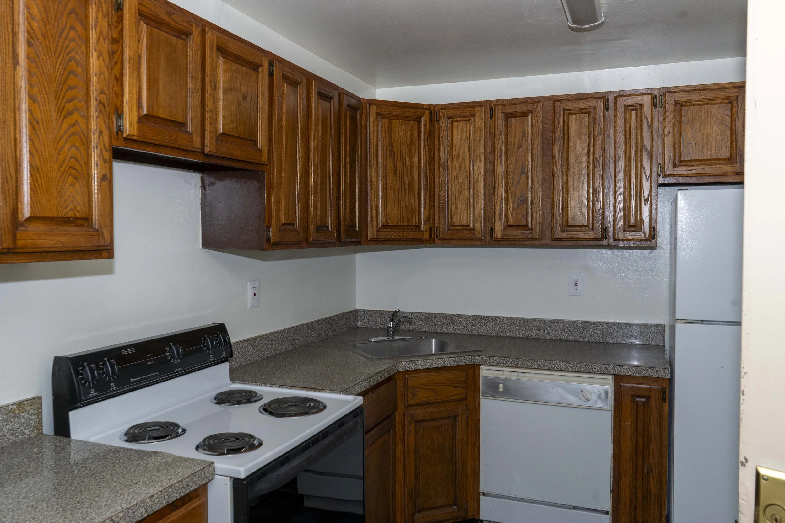 Kitchen with wooden cabinets, a white stove, a small sink, and white appliances including a refrigerator and dishwasher.