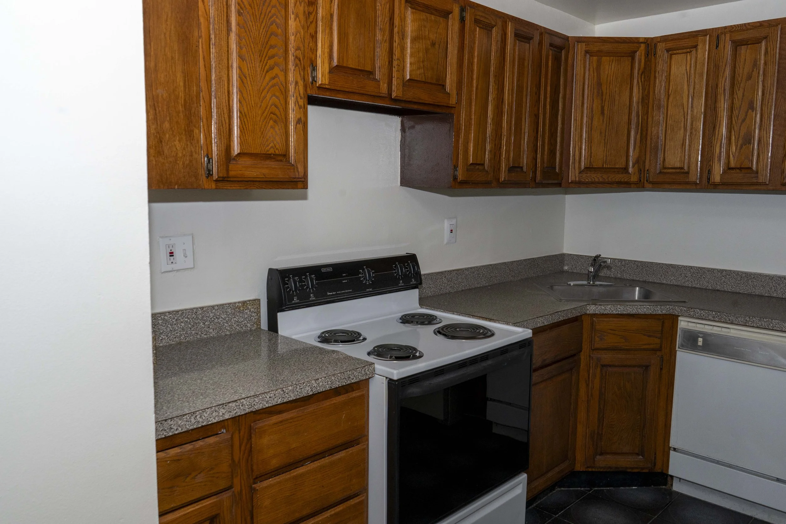 Kitchen with wooden cabinets, a white stove with four burners, a gray countertop, and a stainless steel sink.