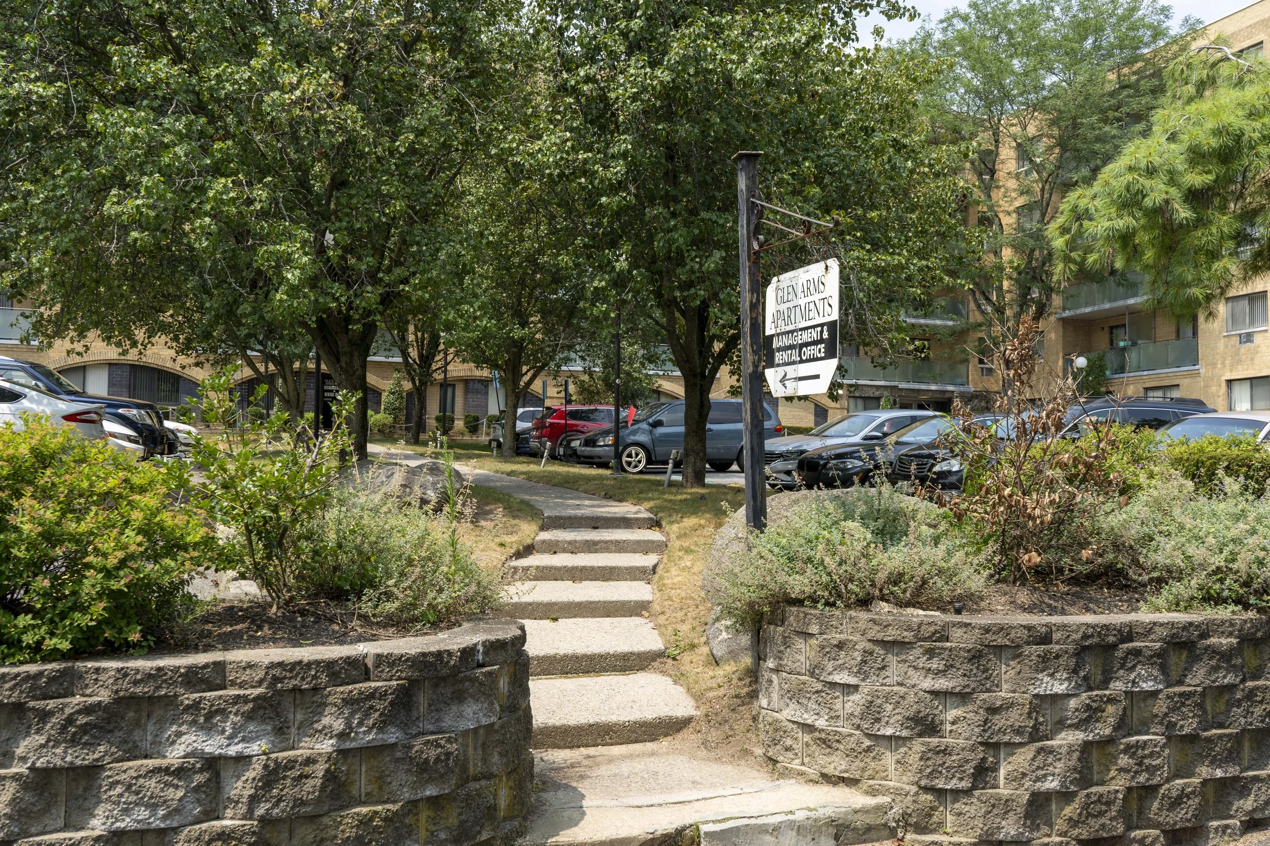 Apartment complex parking lot with cars, trees, bushes, and a sign for Glen Arms Apartments