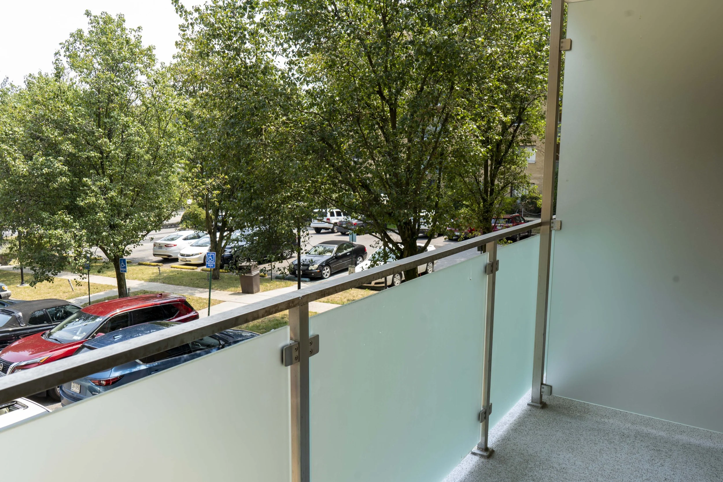 View from a balcony showing parked cars and green trees in a residential parking lot.