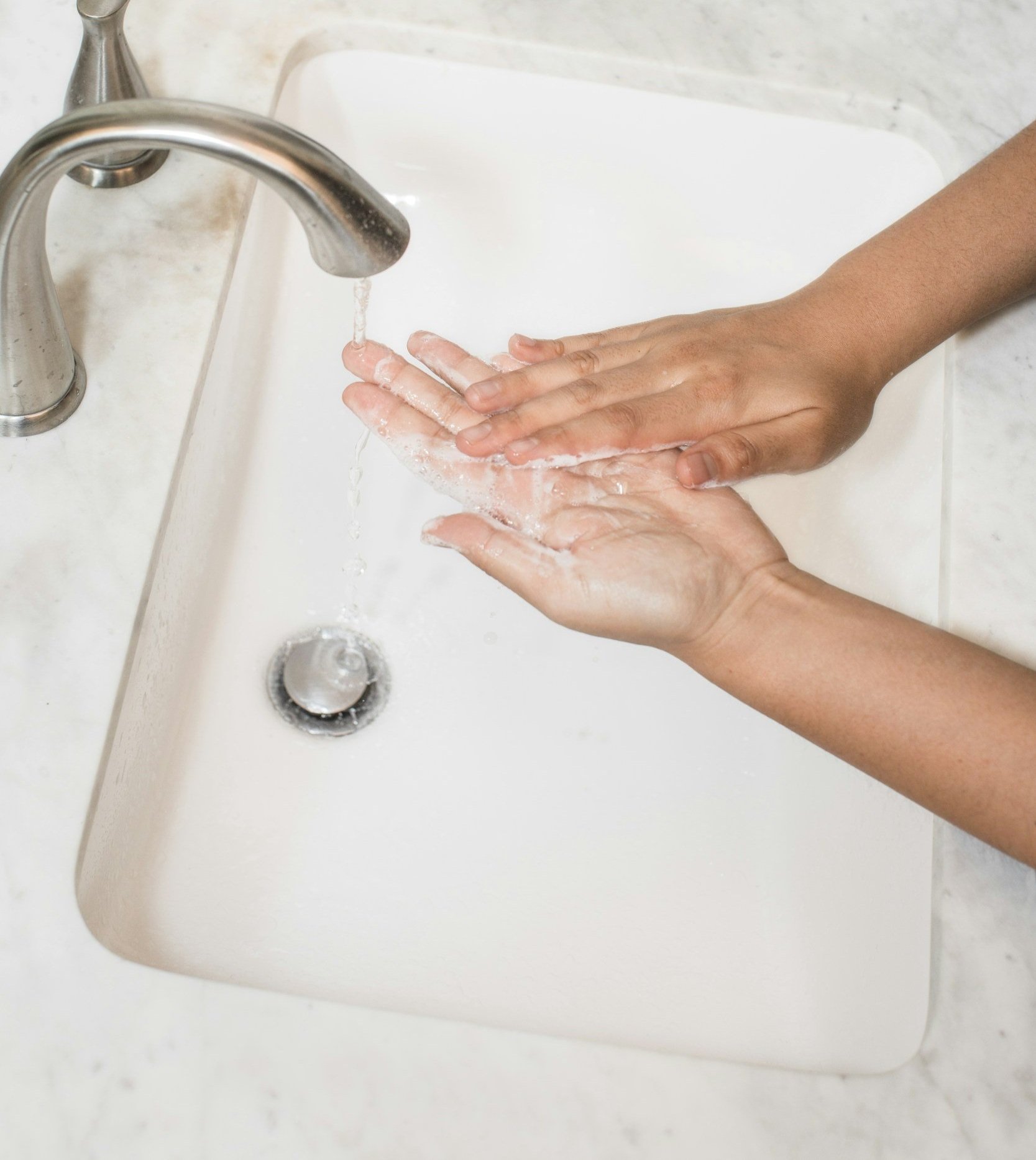 Person washing hands under running water in a sink.