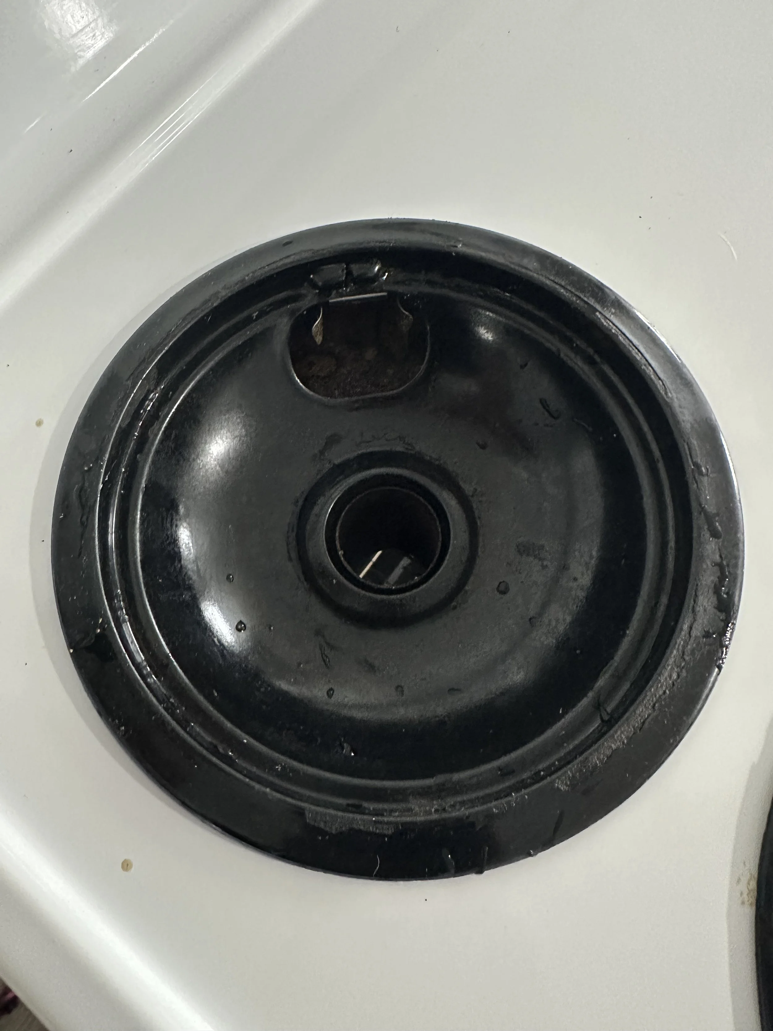 Empty black stove burner cover on white stove surface.