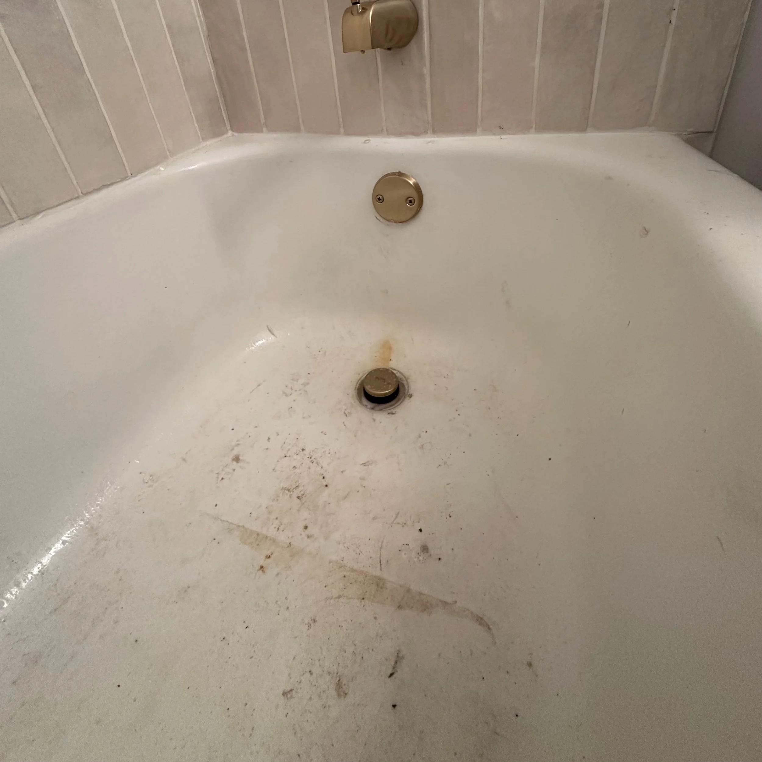 Dirty bathtub with stains and grime, missing faucet, with wall tiles and soap dish visible.