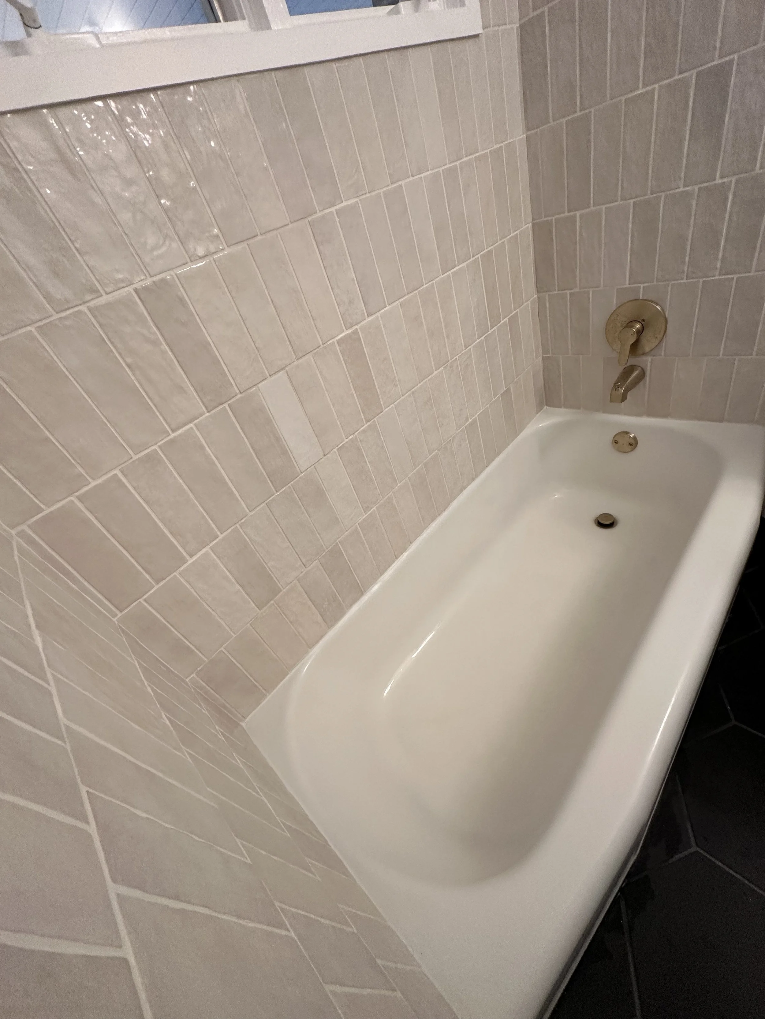 Bathroom with beige tiled walls and a white bathtub, faucet, and drain.