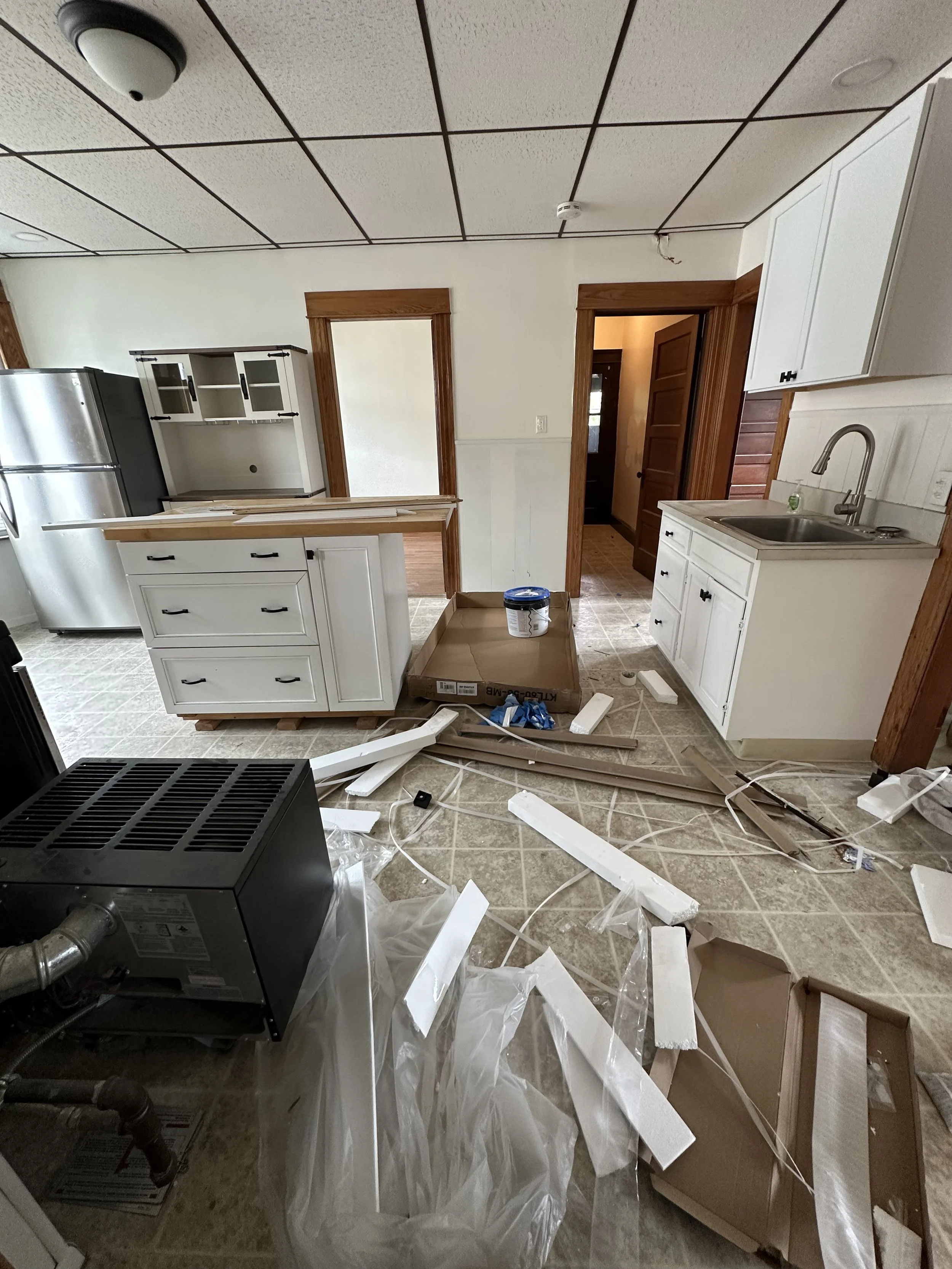 Kitchen with scattered debris, including broken pieces of trim, plastic, and packaging, indicating ongoing renovation or demolition.