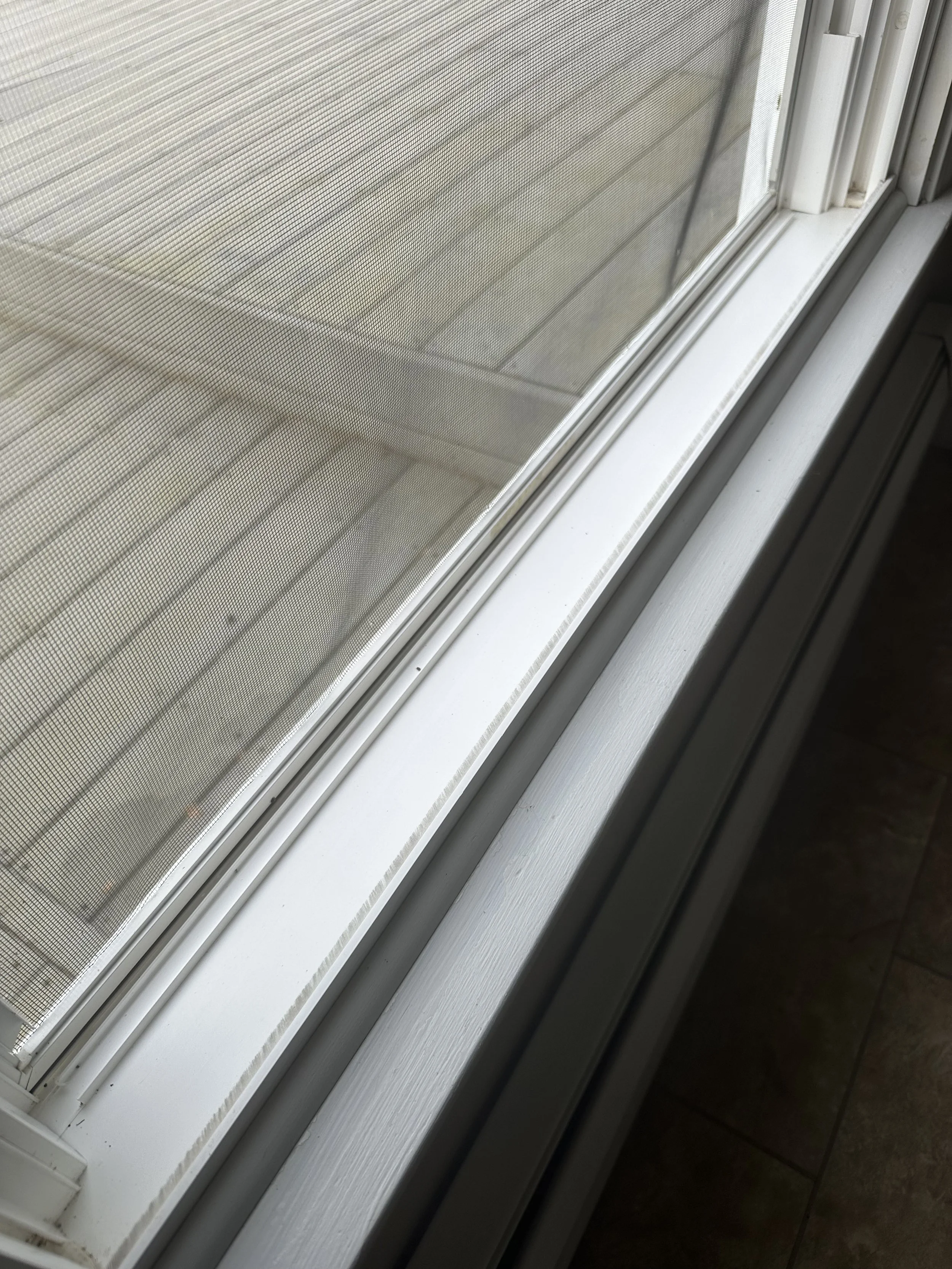 Close-up of a sliding window with a screen, showing the window sill and part of the floor inside a house.