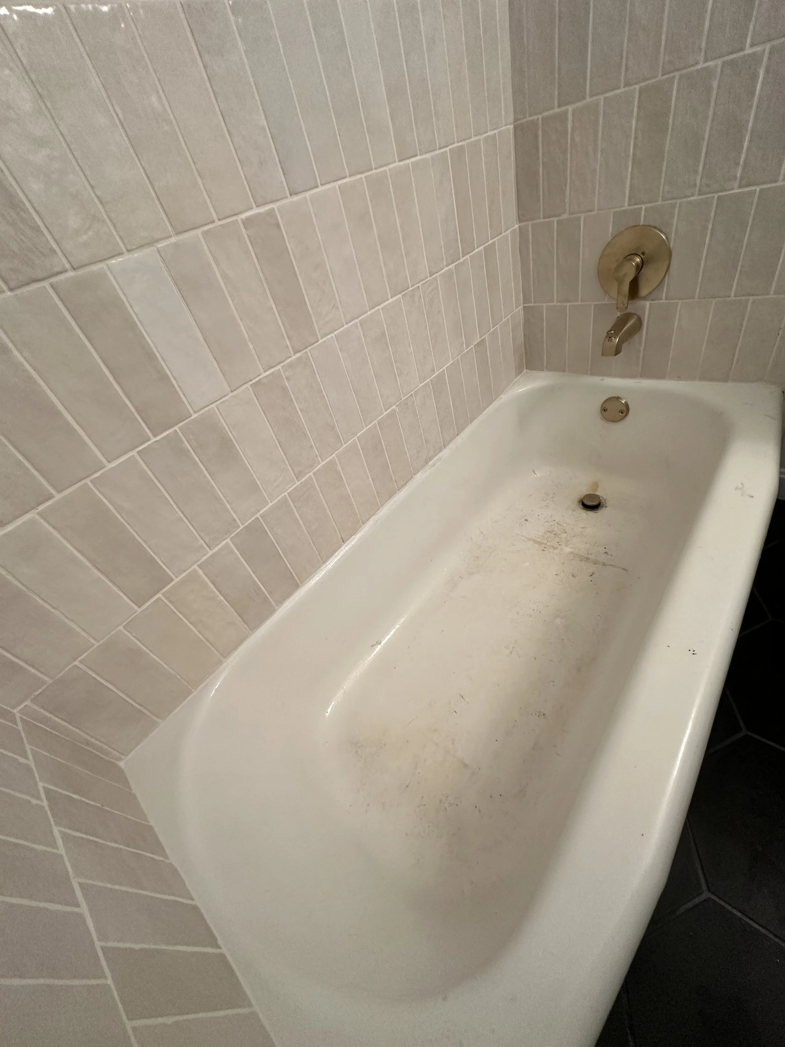 A dirty white bathtub with rust stains, set against beige tiled walls in a bathroom.