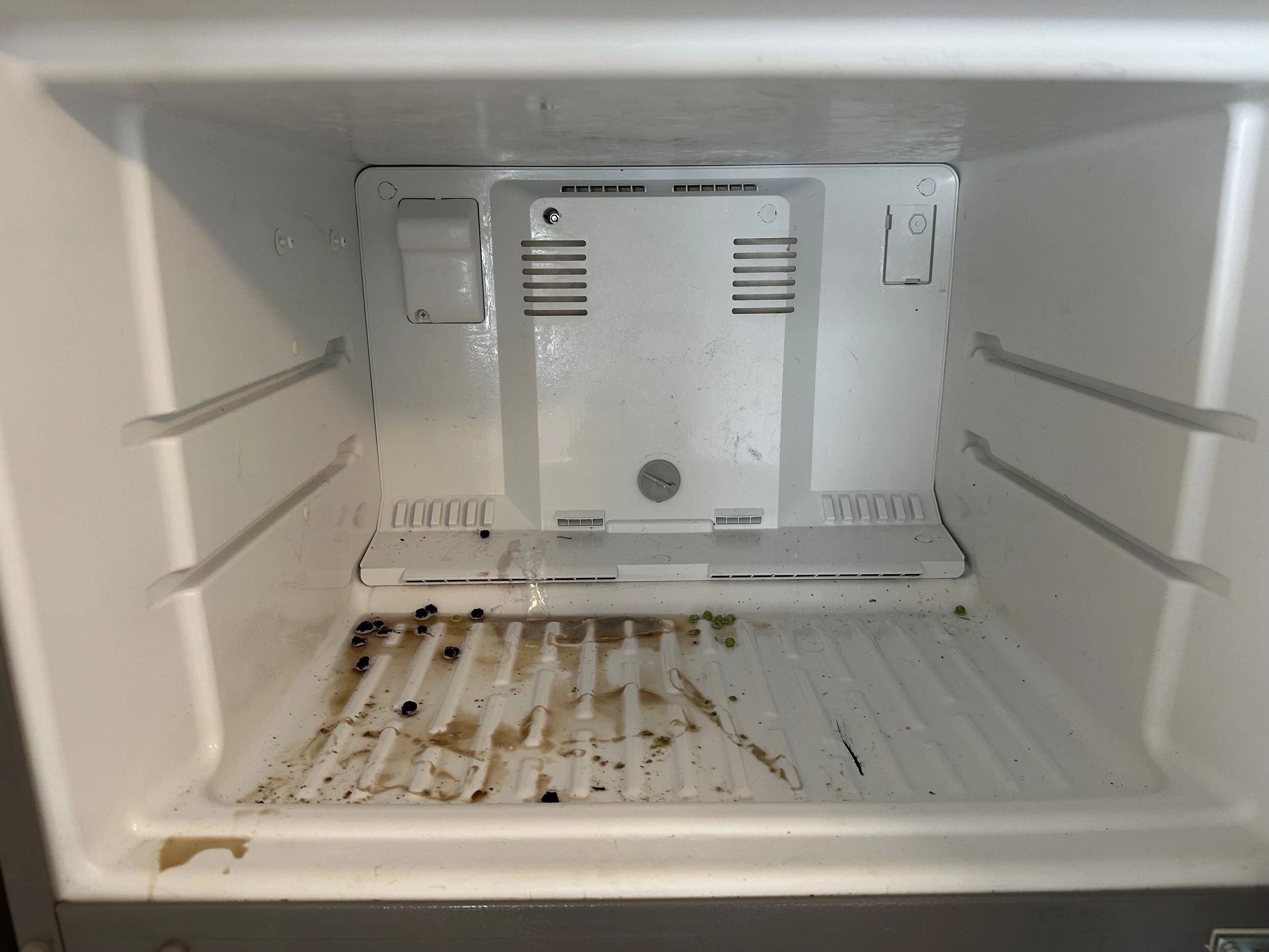 Empty refrigerator with leftover food spills and stains at the bottom.
