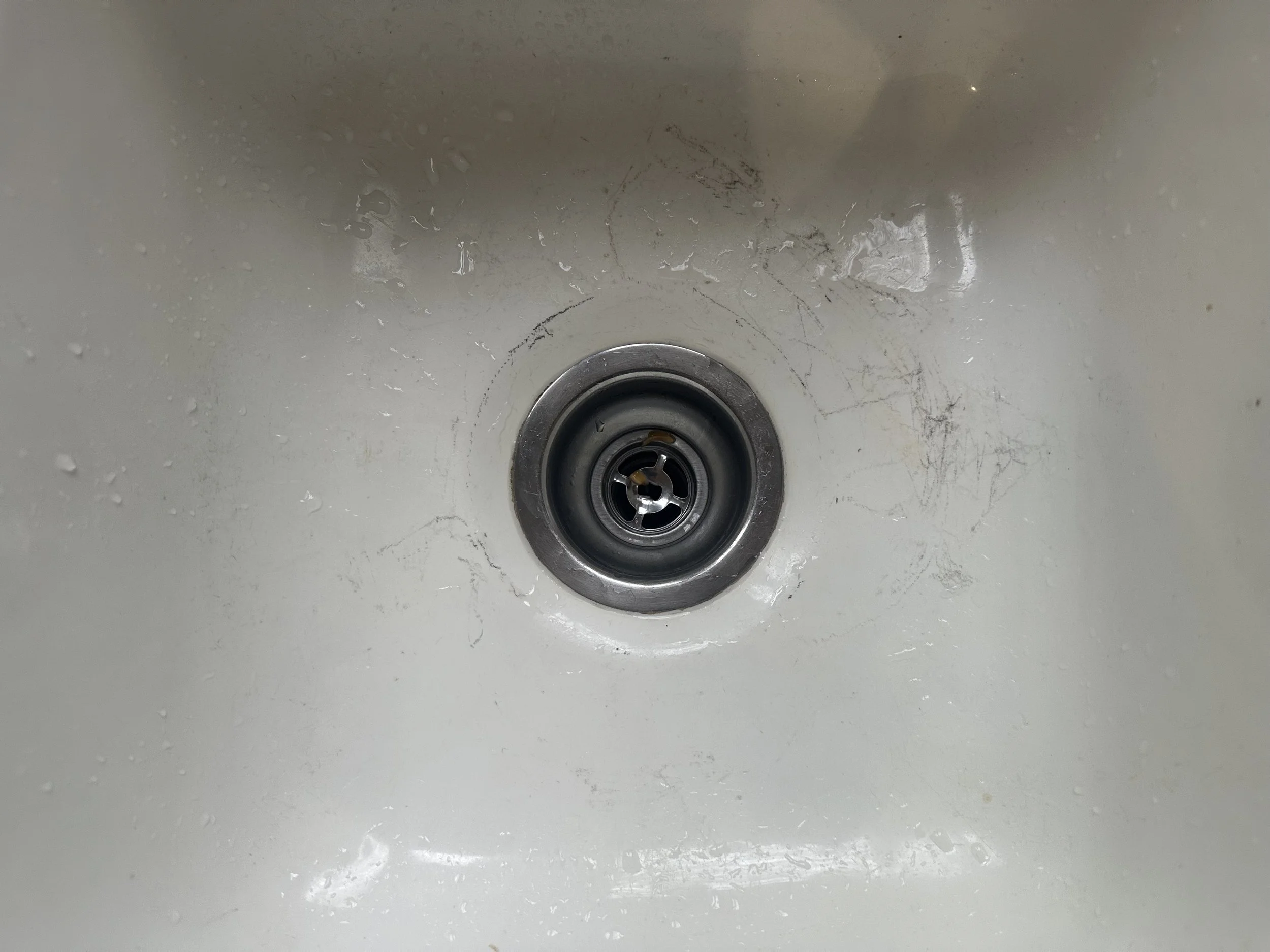 Close-up view of a kitchen sink drain with some scratches and water spots around it.