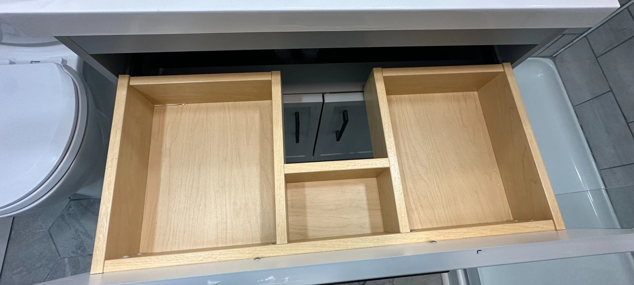 Empty wooden shelves in a kitchen cabinet with a washing machine on the left and tiled floor.