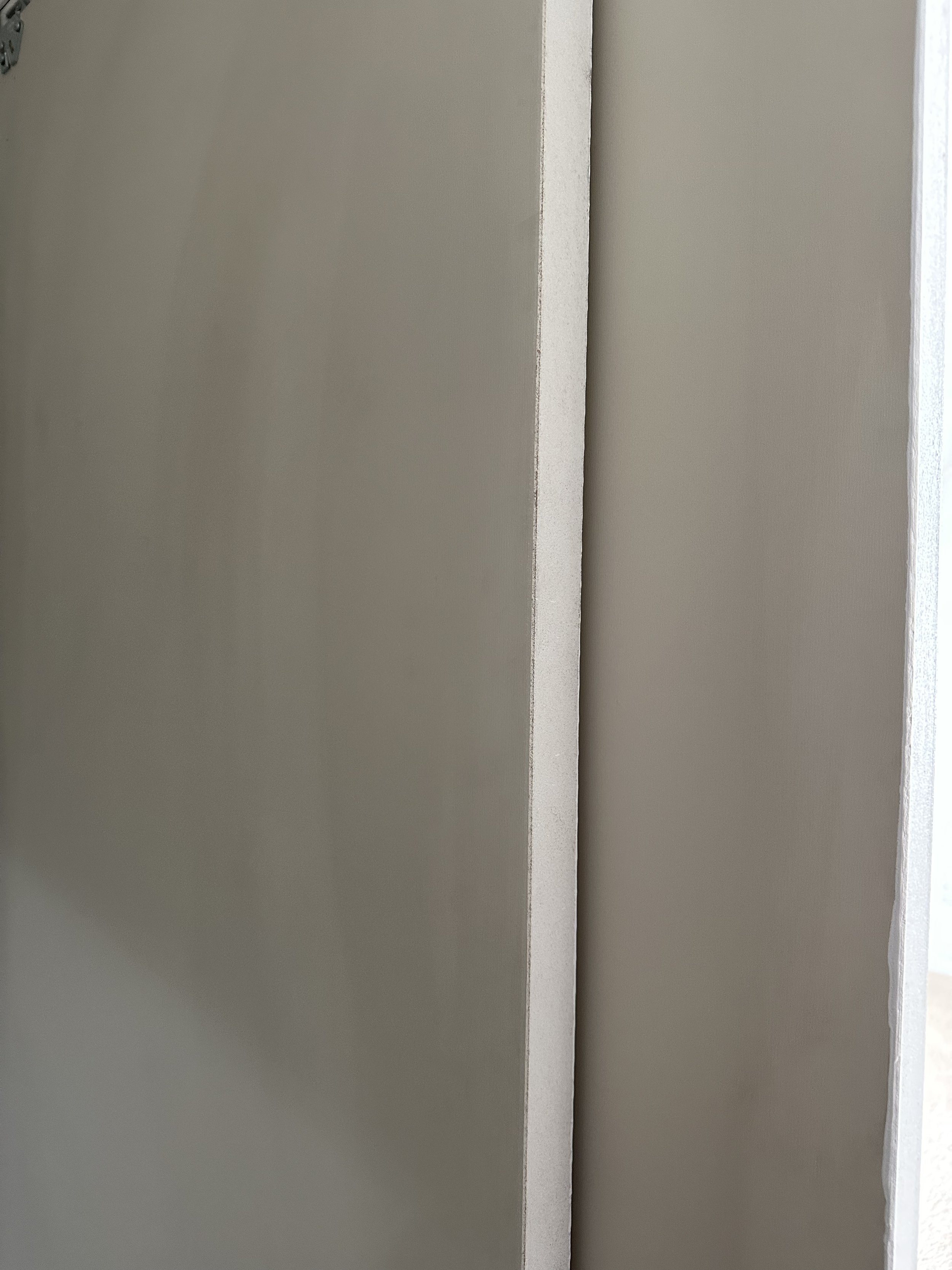 Close-up of a corner between two plain beige walls with a small gap between them.