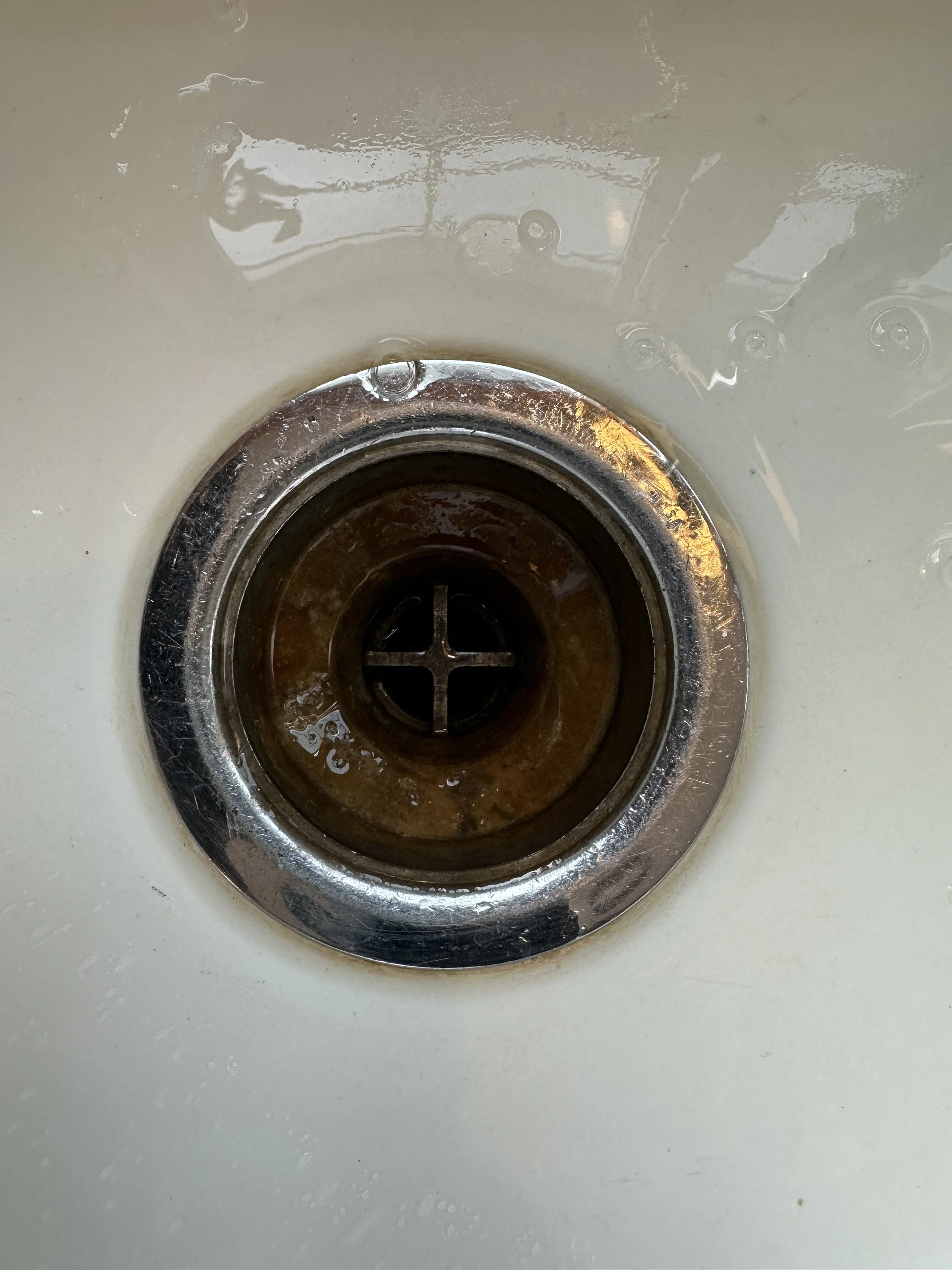 Close-up view of a kitchen sink drain with brown discoloration and water around it.