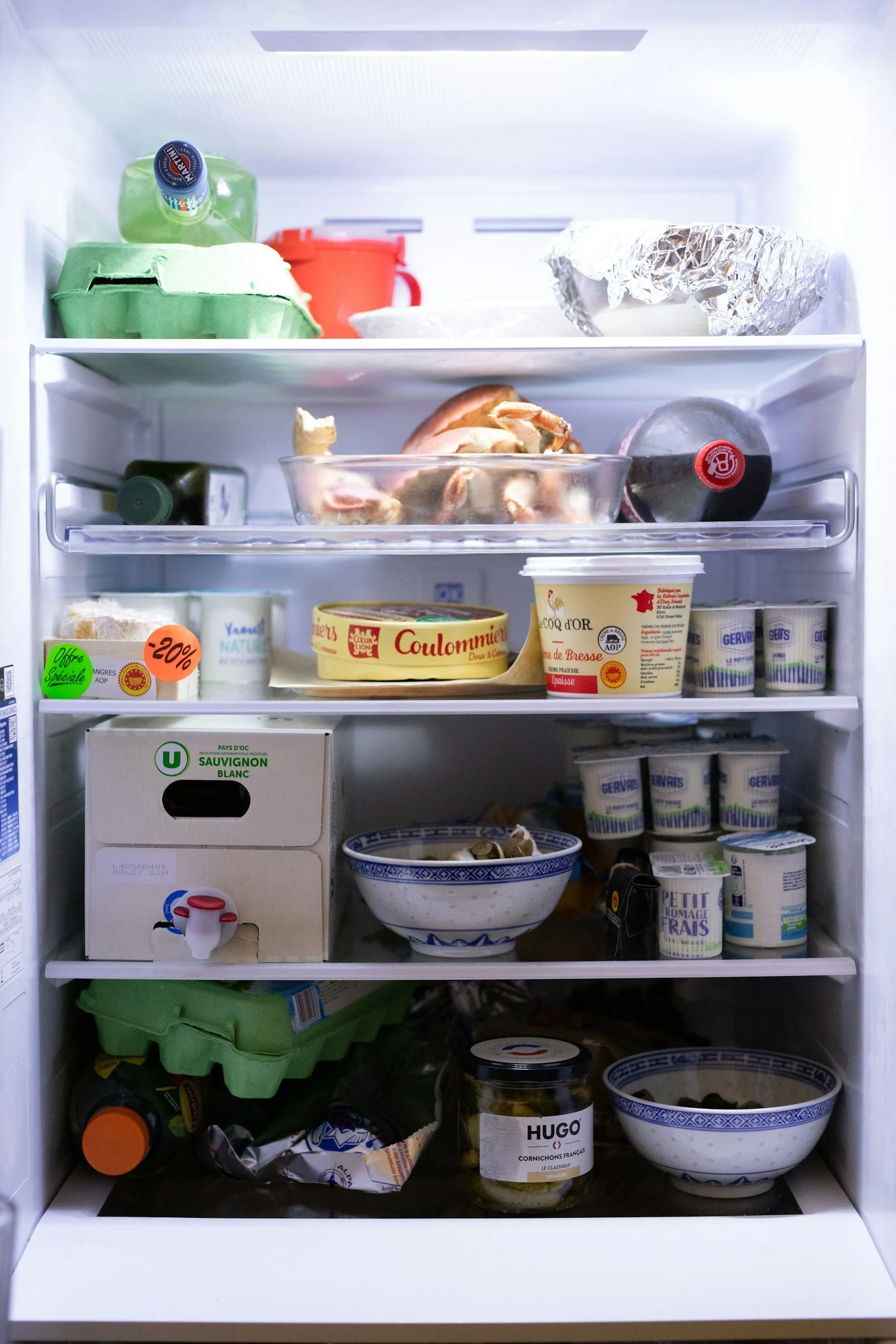 Inside a refrigerator, with various food items including eggs, yogurt, condiments, a jar of pickles, and leftover dishes.
