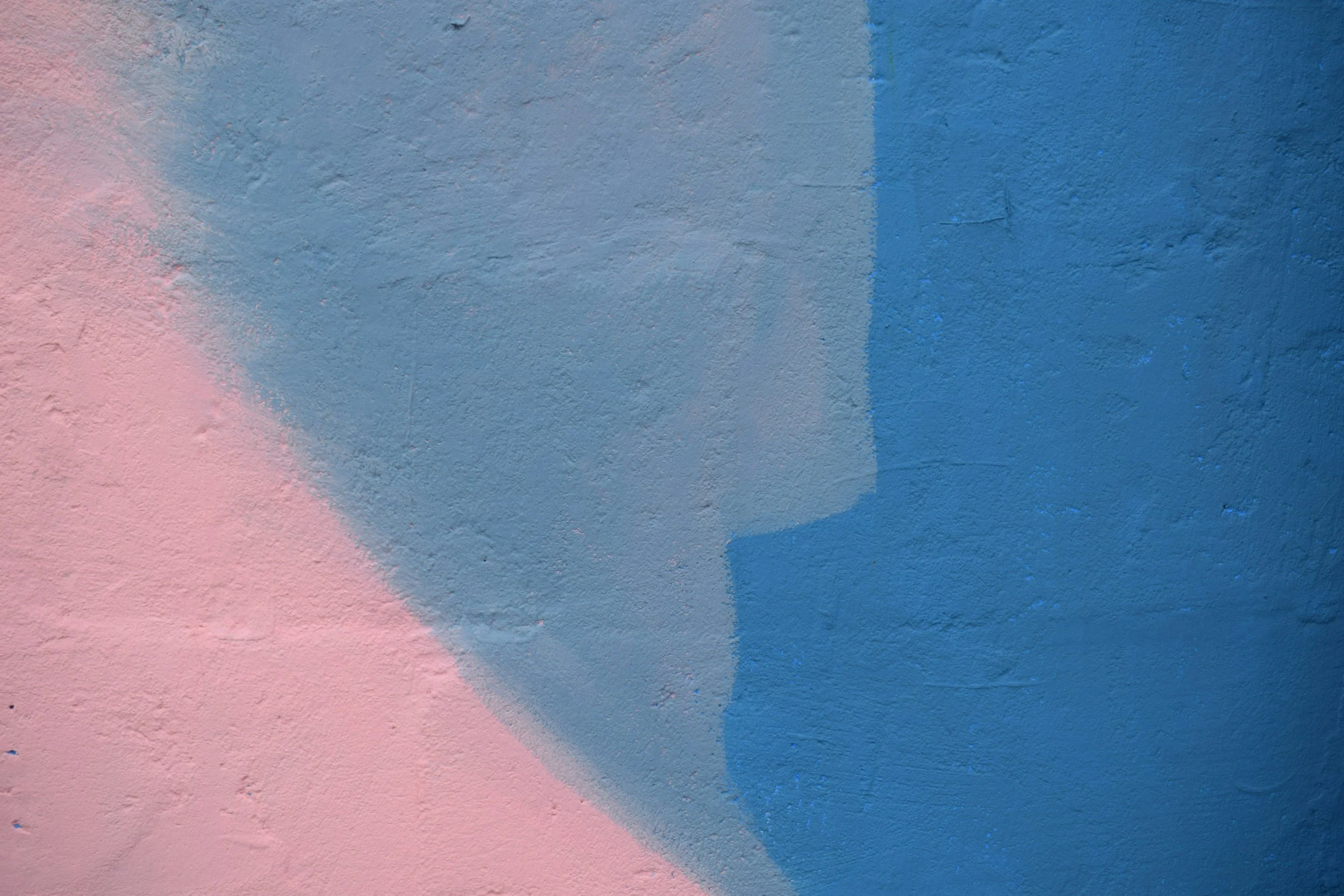 Close-up of a wall painted with overlapping sections of pastel pink, blue, and gray colors.