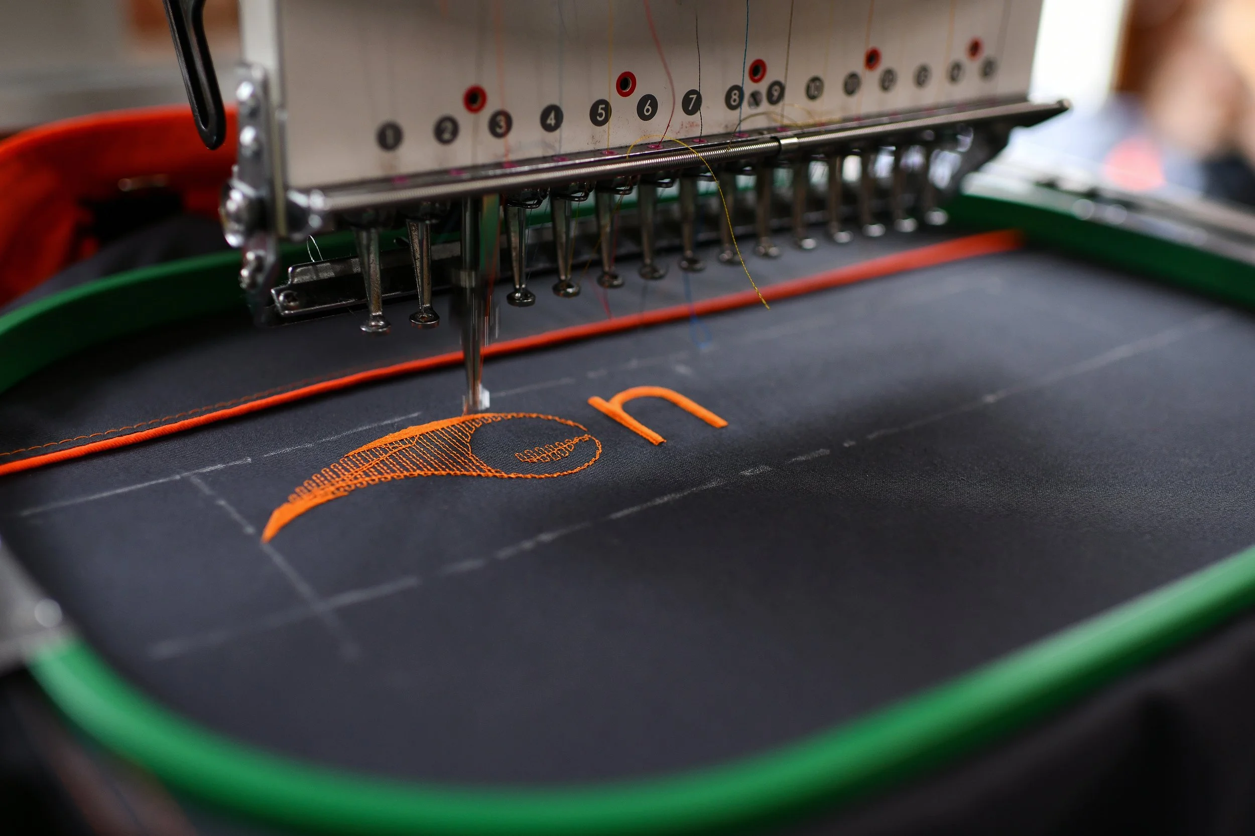 Close-up of an embroidery machine stitching an orange design onto black fabric.