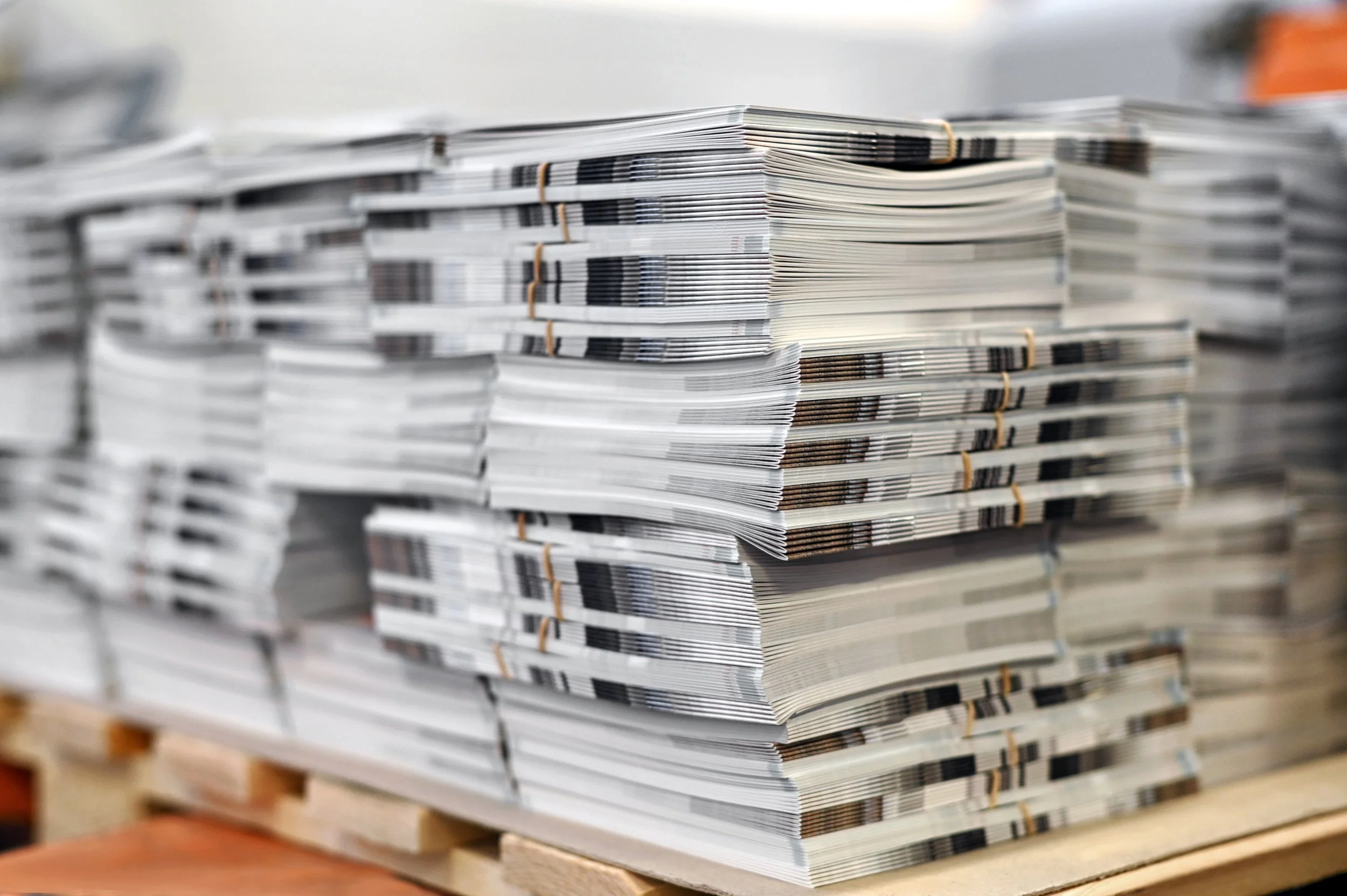 Multiple stacks of newspapers arranged neatly on a wooden pallet.