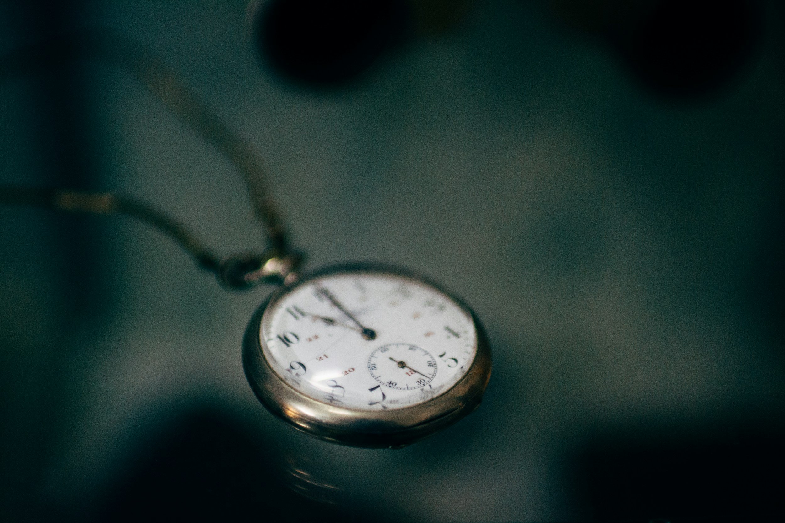 Close-up of a vintage pocket watch with a white face, black numerals, and a smaller seconds dial, hanging from a chain.