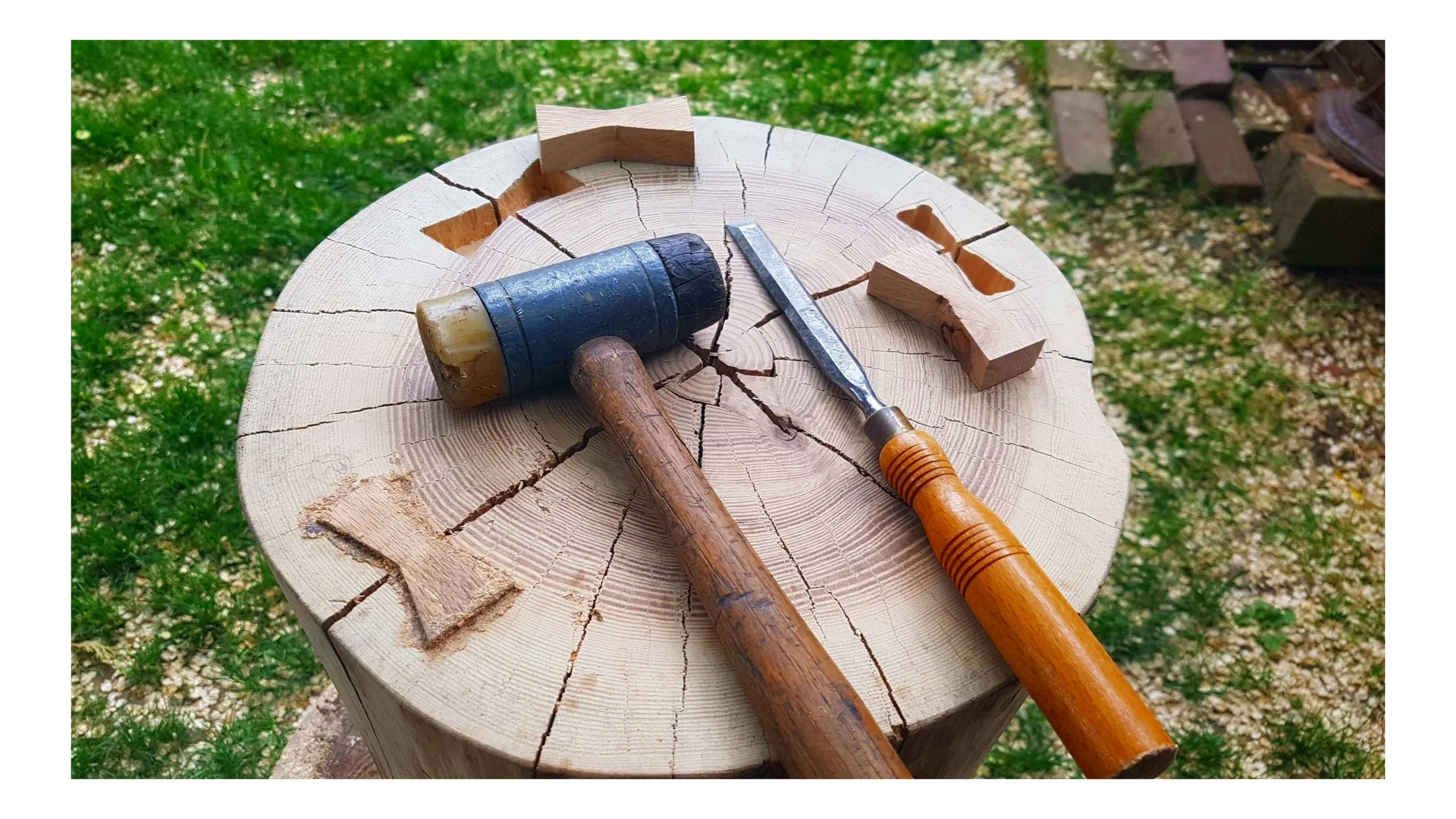 A wooden carving mallet, a chisel, and wooden pieces on a tree stump outdoors.