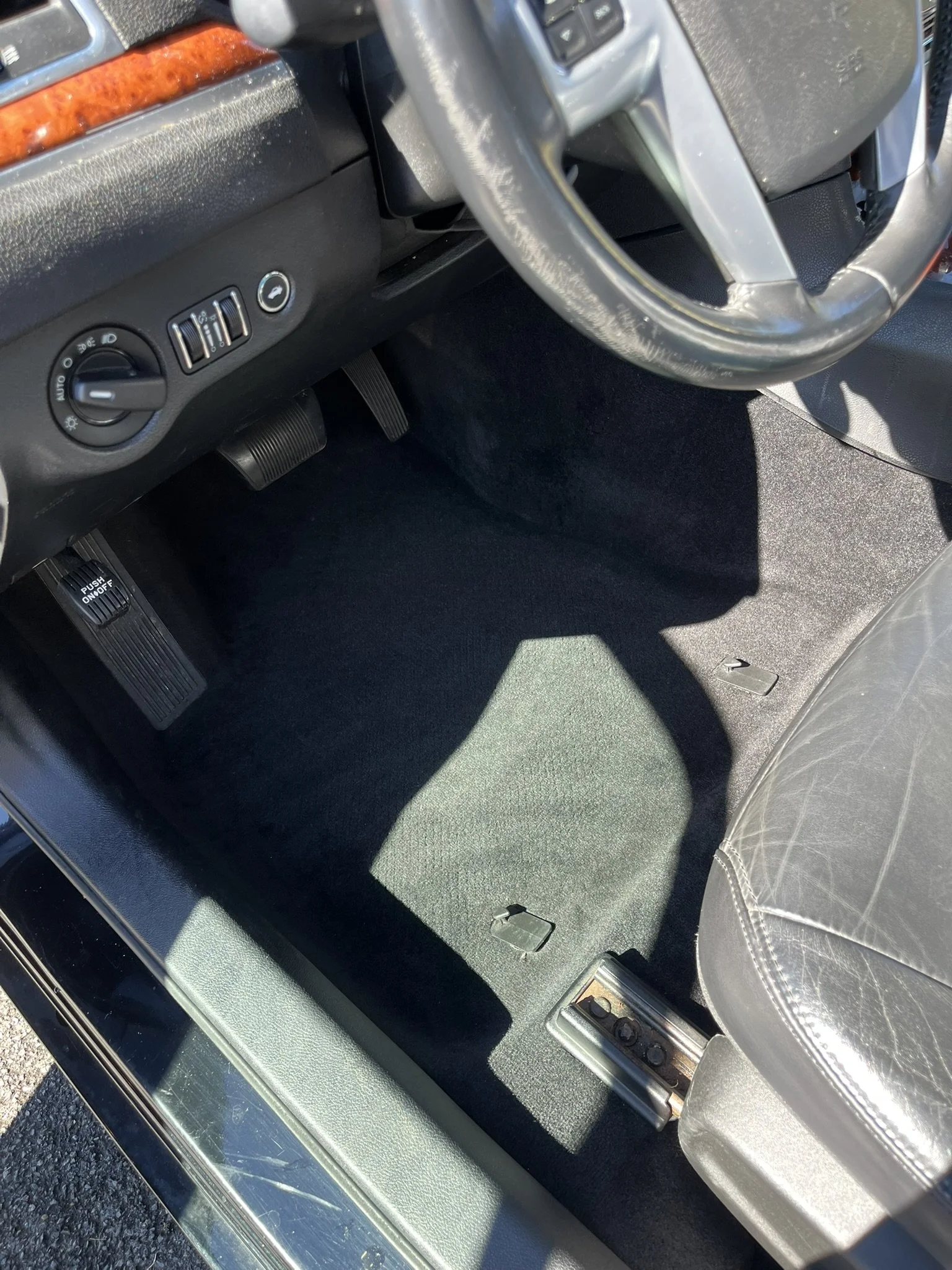 Interior of a car showing the driver's side footwell with pedals, under the steering wheel, and part of the driver's seat.