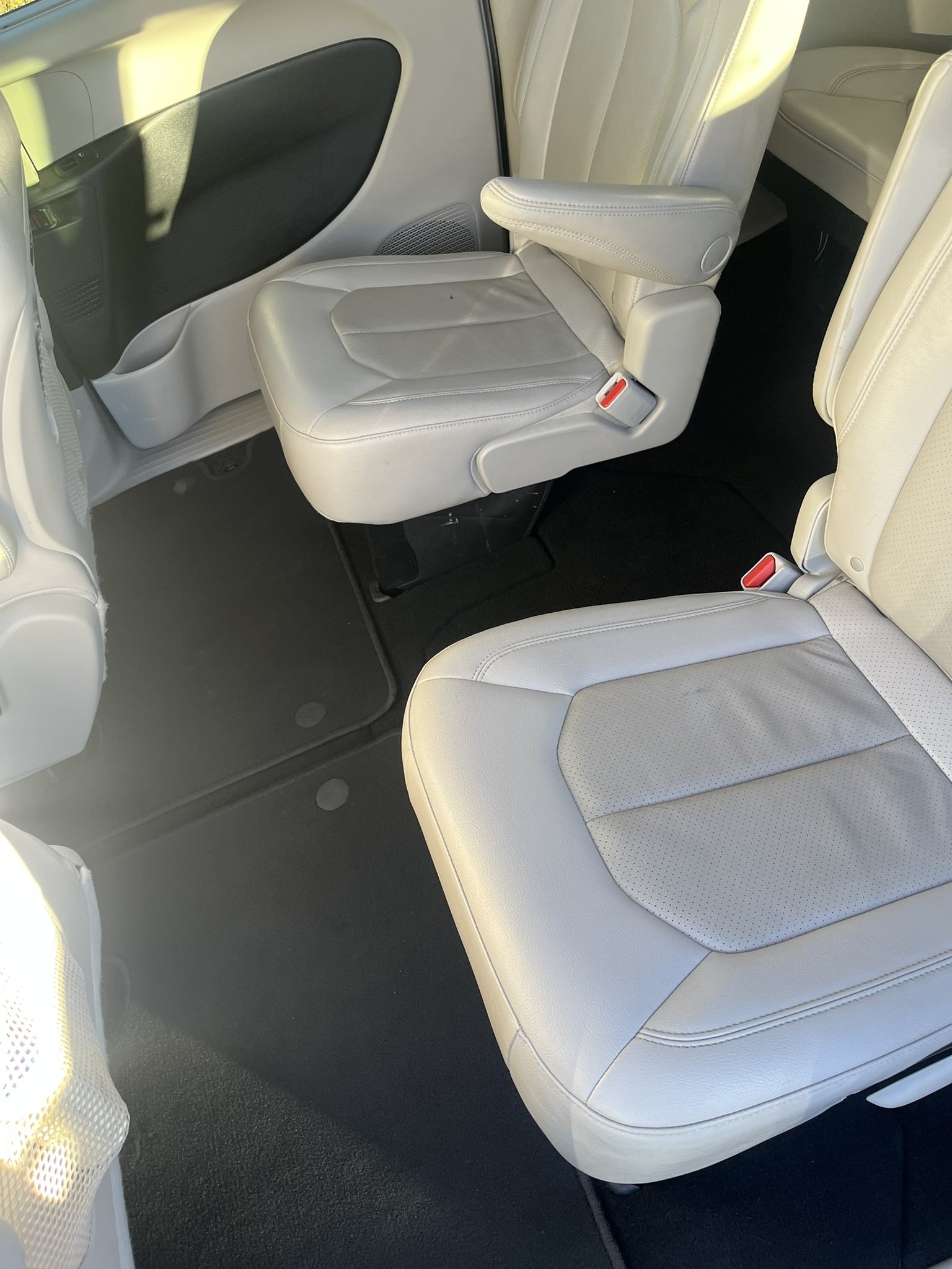 The interior of a vehicle showing three ivory-colored leather seats, with the middle seat folded down to reveal a tray table, and the floor is covered with black carpet.