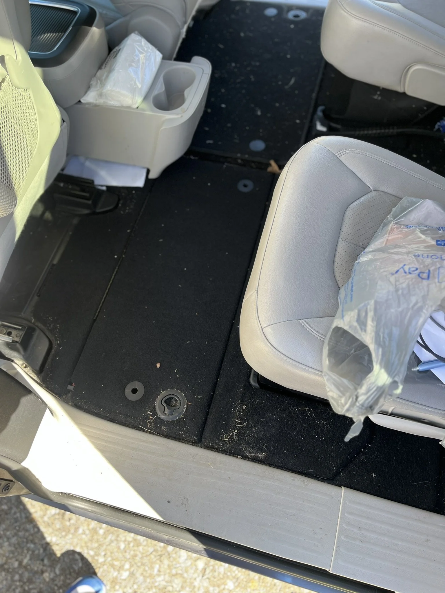 Inside a vehicle showing the passenger side floor area with some scattered debris, a black floor mat, and a portion of a white leather seat with a plastic bag hanging on the side.