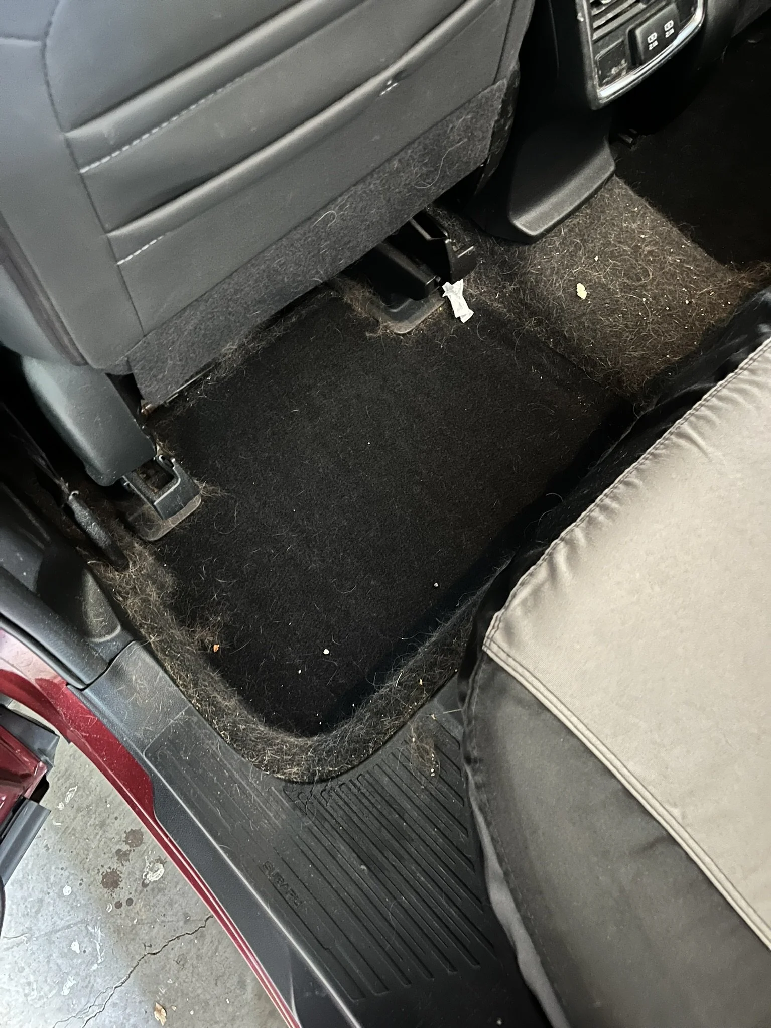 Inside a vehicle, showing the rear passenger area with a dirty and dusty floor mat, spent tissues, and part of the seatback.