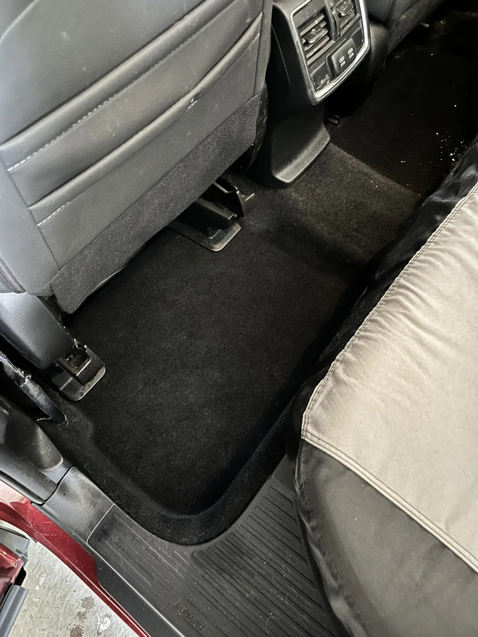 The interior of a vehicle showing the back of the front passenger seat, a floor mat, and part of a person's leg and shoe.