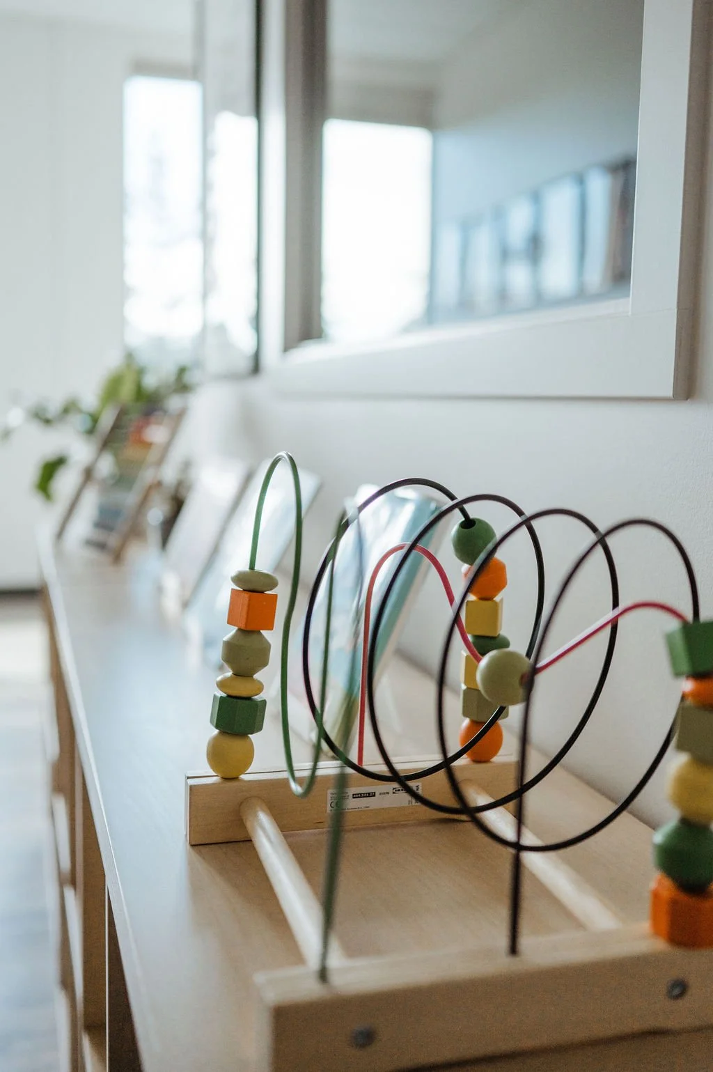 Colorful wooden bead wire maze toys on a wooden surface in a bright room.