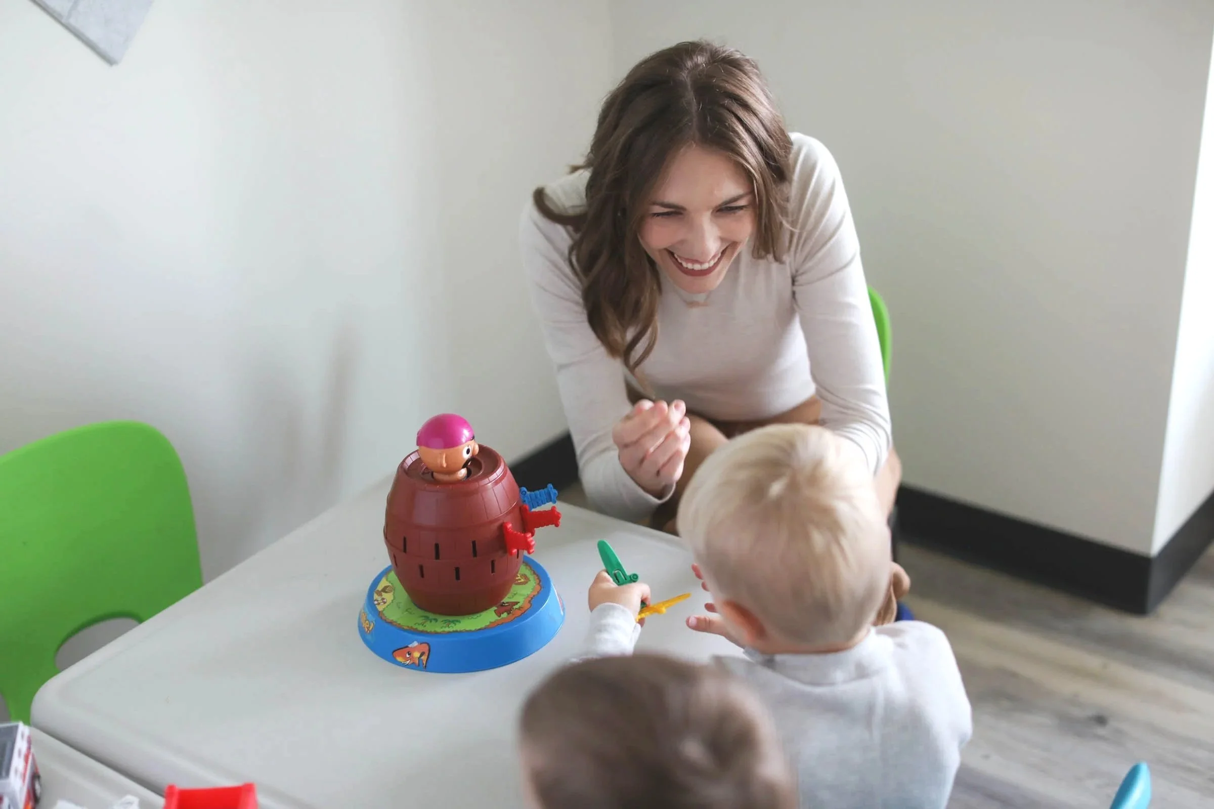 A woman playing a game with two children at a table, with a pink and brown game piece on a blue and brown game board.