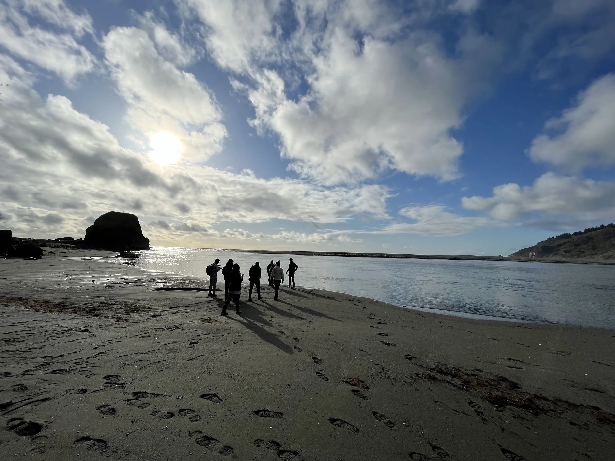 A group of colleagues gather on a beach where the Klamath River empties into the ocean, during a team retreat.