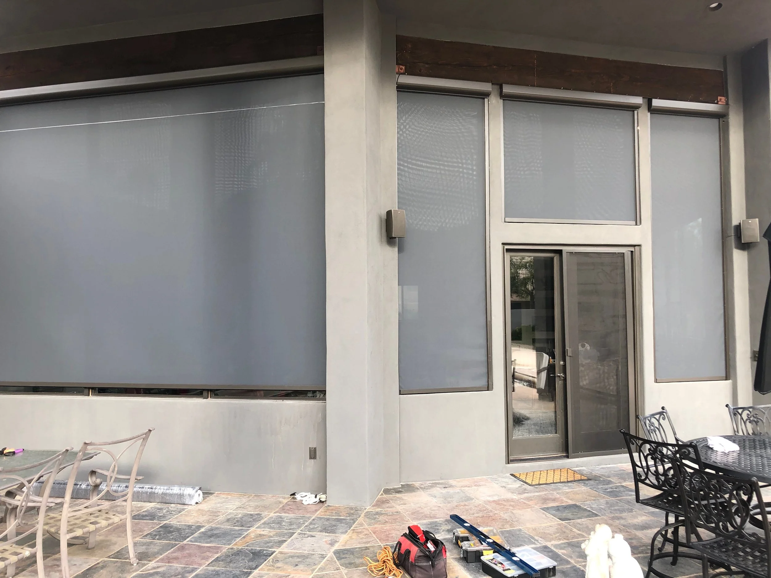 Outdoor patio area with tools and furniture near a building with gray walls and metal-framed windows and doors.
