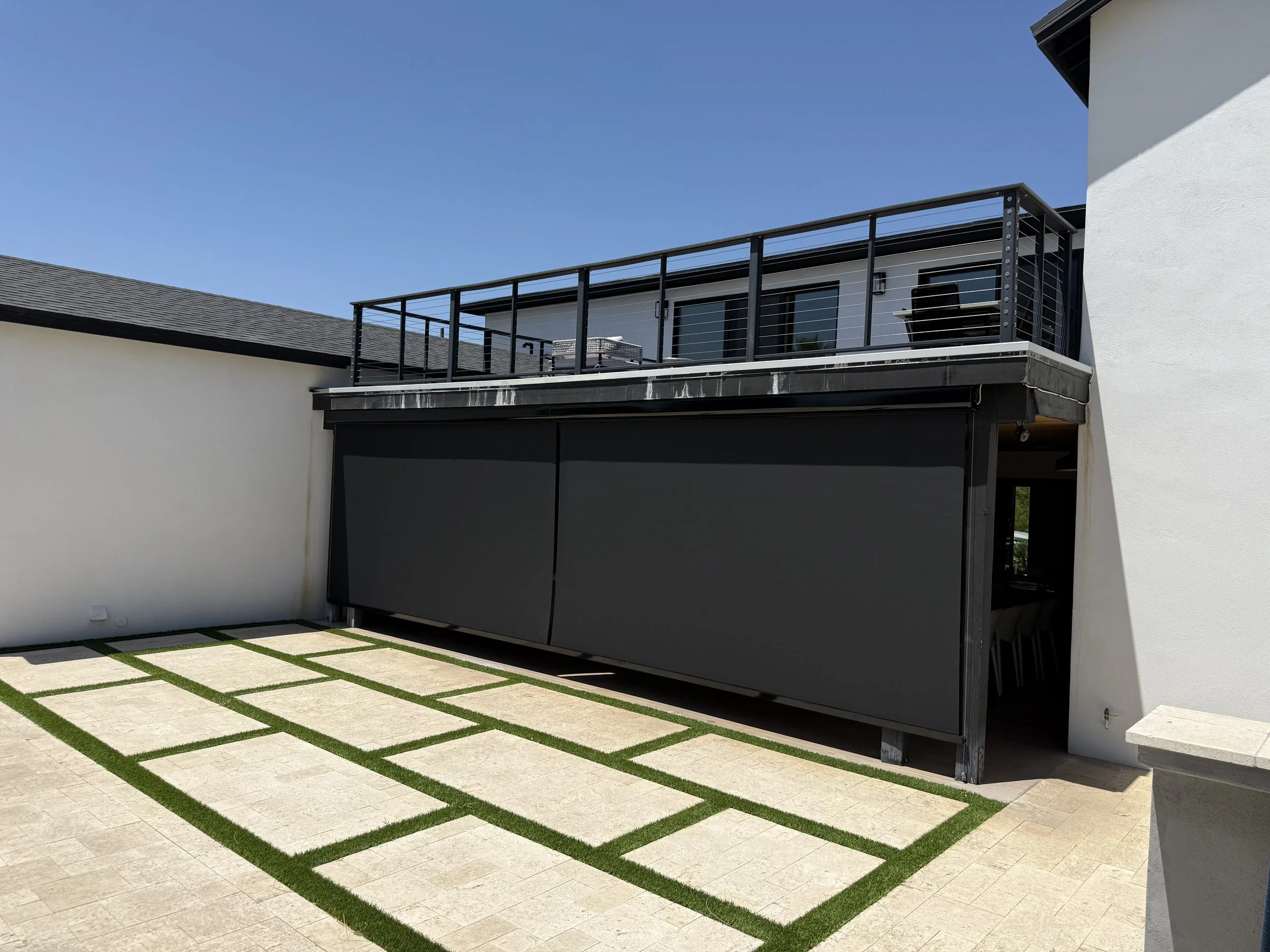 Modern outdoor space with paved area, white walls, and a new black balcony with railing on the second floor of a white house.
