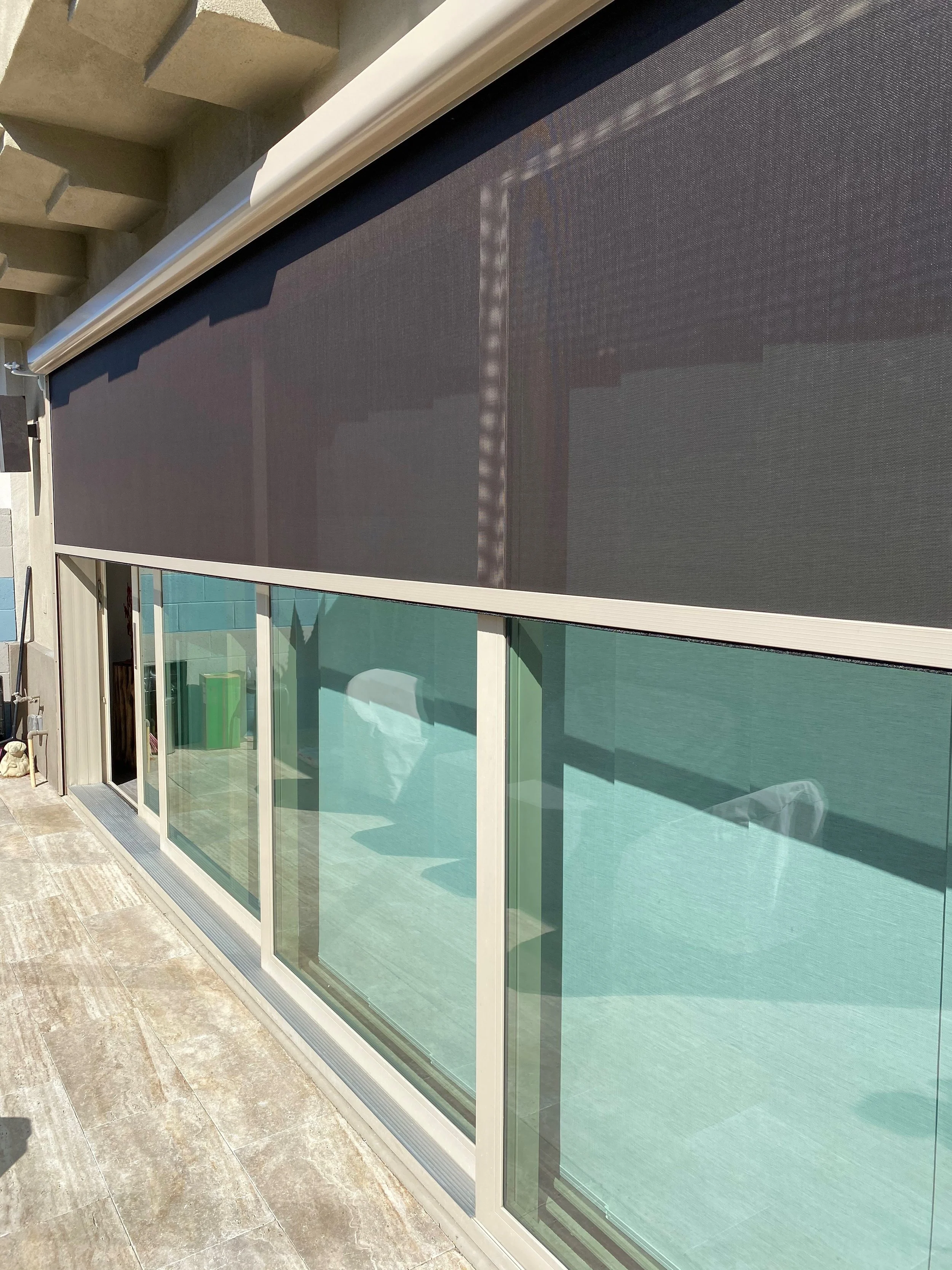 Exterior of a residential building with sliding glass doors, a mesh screen in front of the doors, and an outdoor patio area with tiled flooring.
